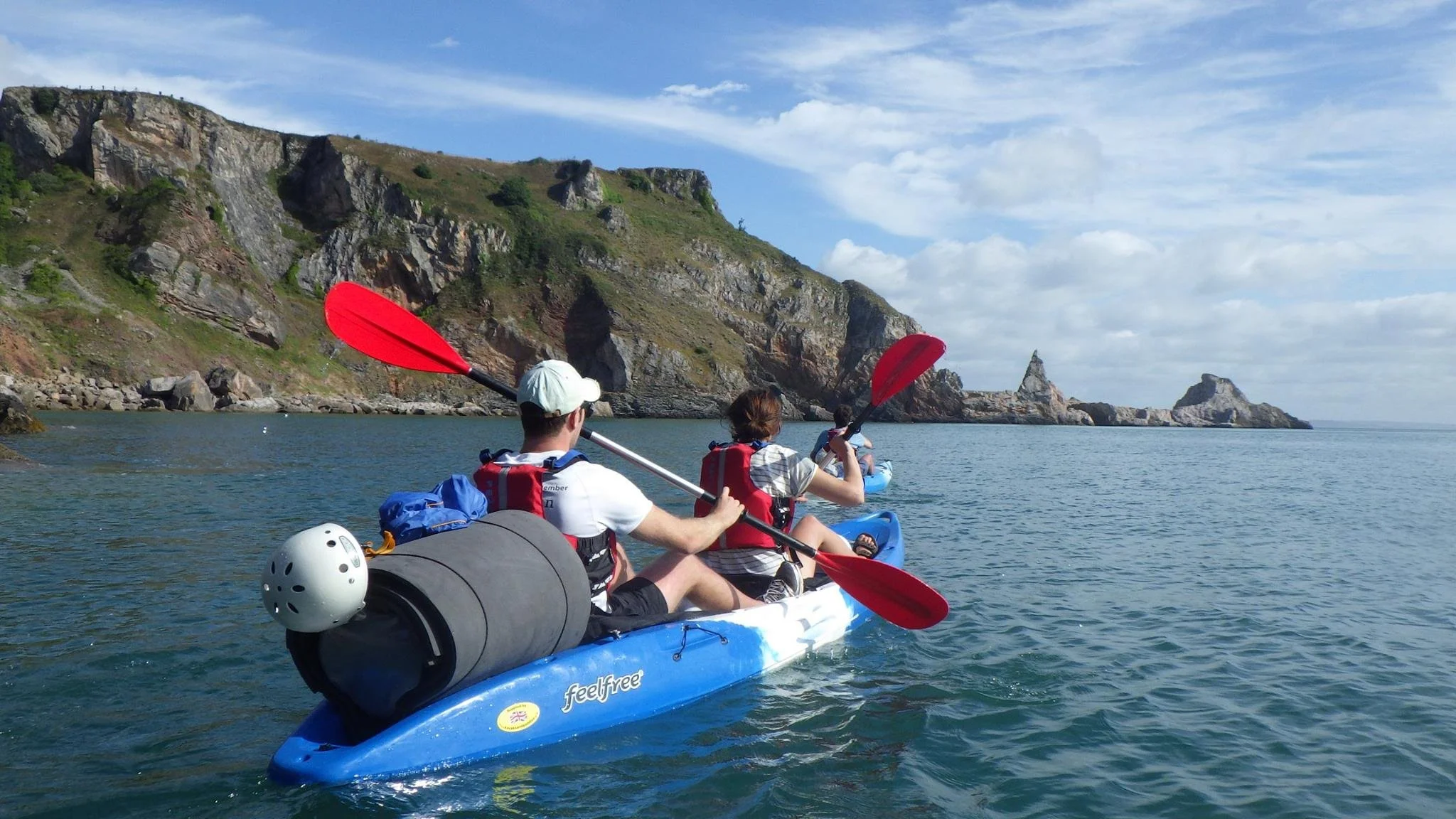 People kayaking on a body of water near rocky cliffs under a partly cloudy sky.