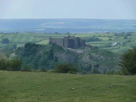A landscape view of an ancient stone castle on a hill overlooking green fields and distant hills under a blue sky.