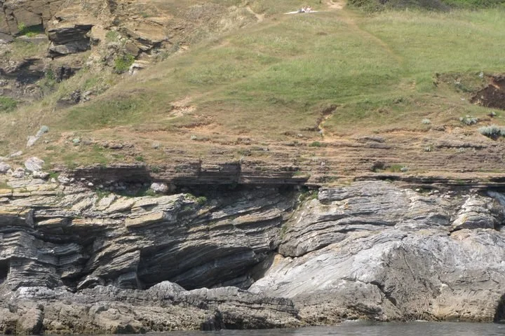 Cliffside with layered rock formations and grass-covered hilltop