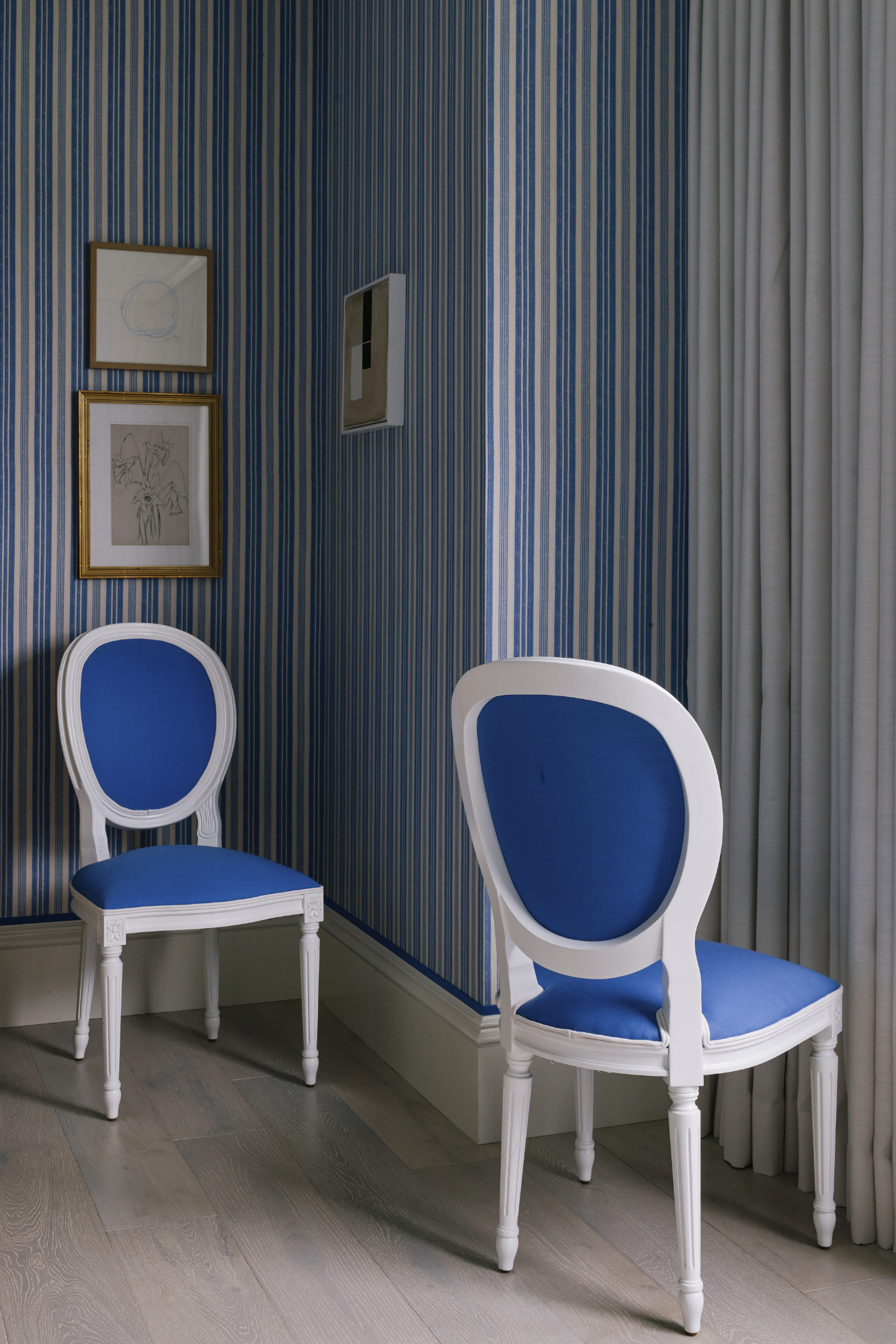 Interior with blue and white striped wallpaper, two white and blue chairs, and framed artwork on the wall.