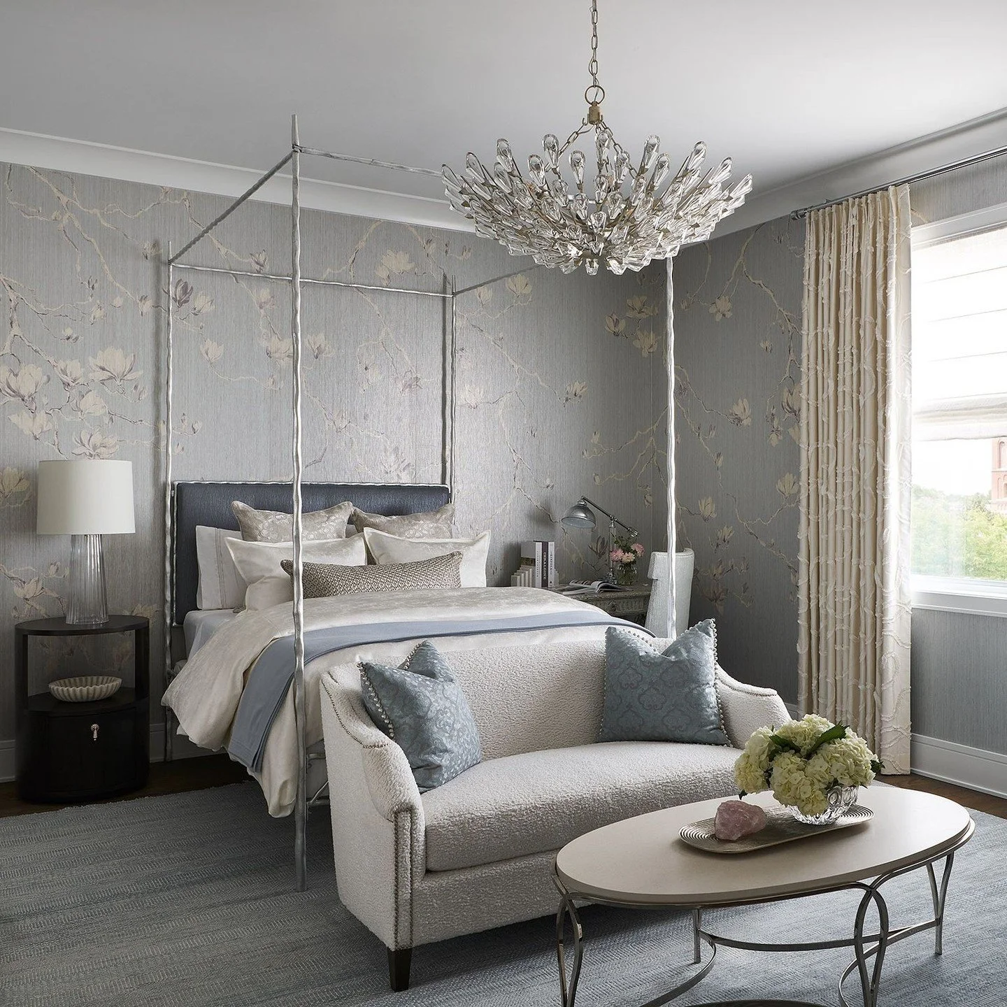 Elegant bedroom with a four-poster bed, a sofa with pillows, a chandelier, a window with curtains, and decorative touches.