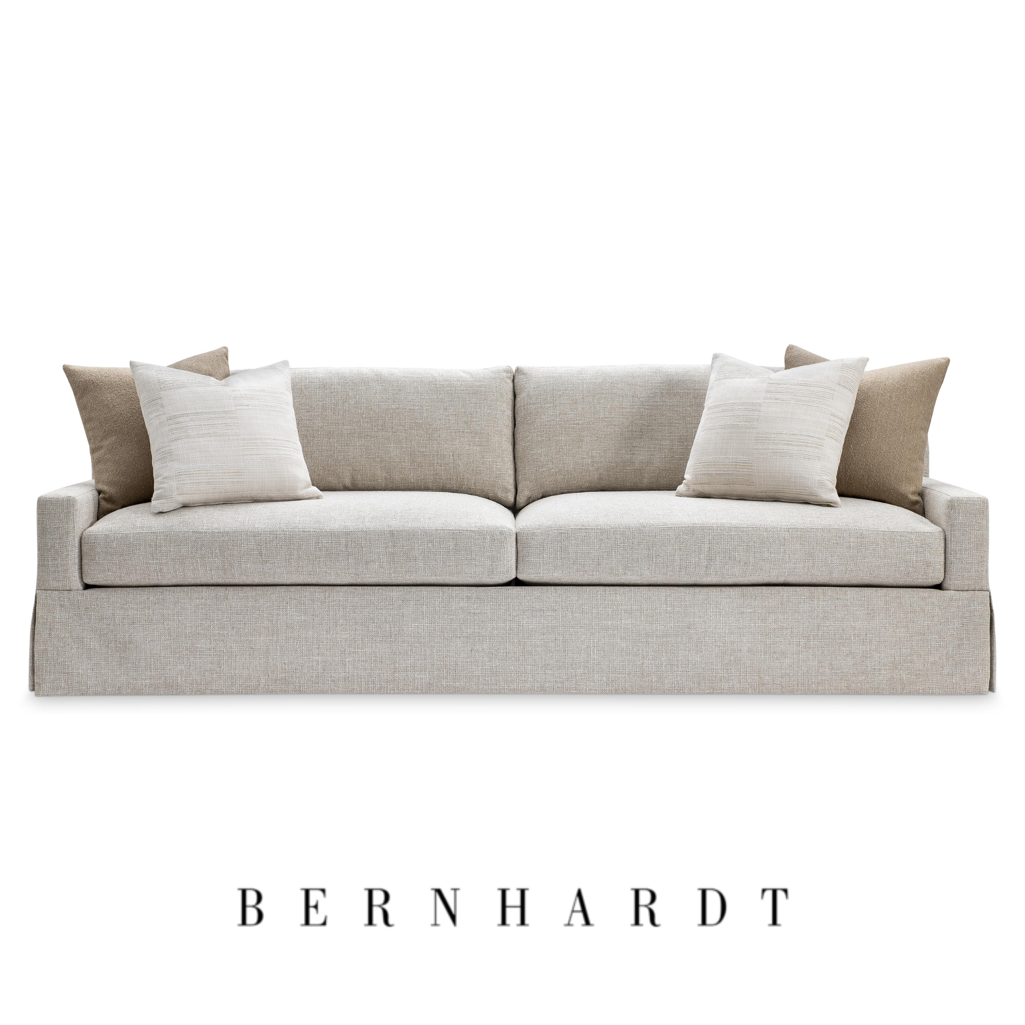 A modern beige sofa with four pillows, two white and two beige, from Bernhardt Furniture.