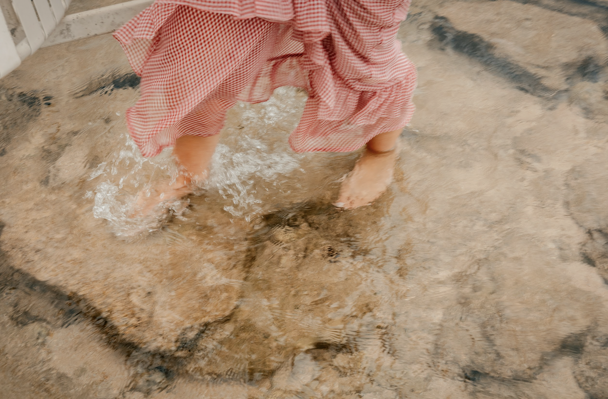 Children playing in water, barefoot, on a concrete surface with a small puddle.