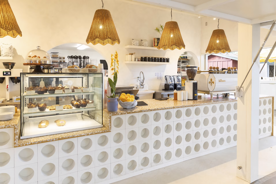 Café counter with pastries and coffee machines, illuminated by hanging wicker lamps.