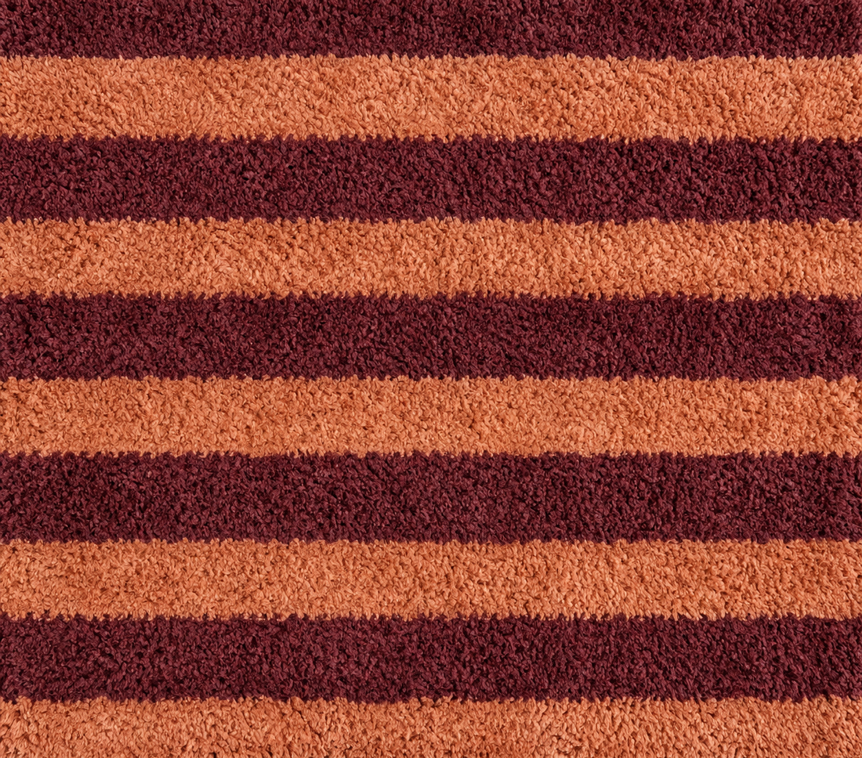 Close-up of a striped carpet with alternating dark red and orange stripes.
