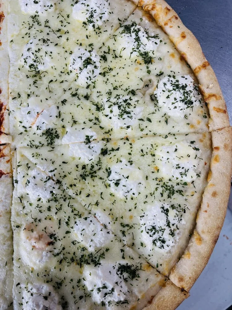 Close-up of a cheese pizza topped with shredded cheese, dollops of ricotta, and sprinkled with chopped herbs.