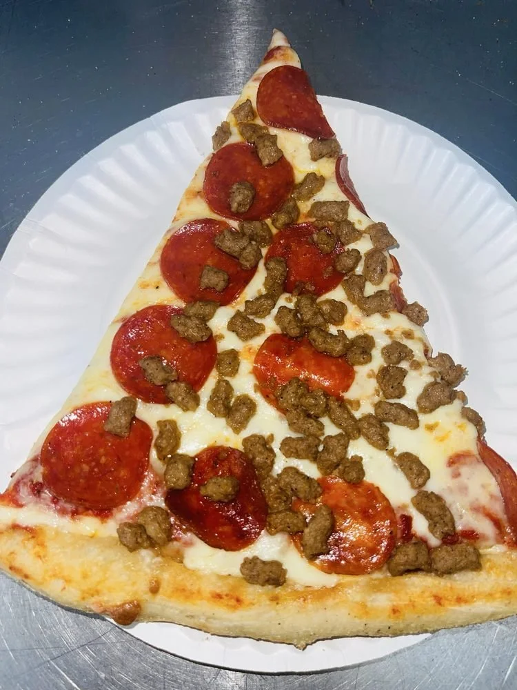 A slice of pepperoni pizza with ground beef on top served on a white paper plate.