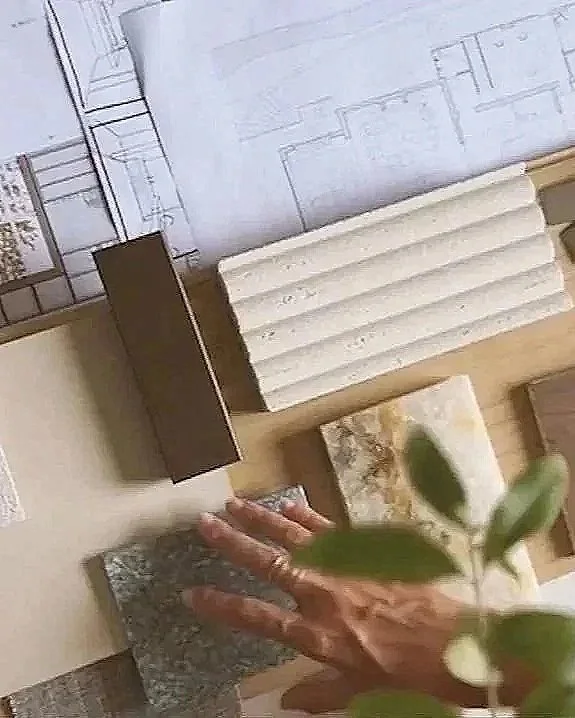Une main est en train de toucher un plan ou une maquette en miniature, avec divers matériaux et plans en arrière-plan, peut-être dans un contexte de conception ou de modélisation.