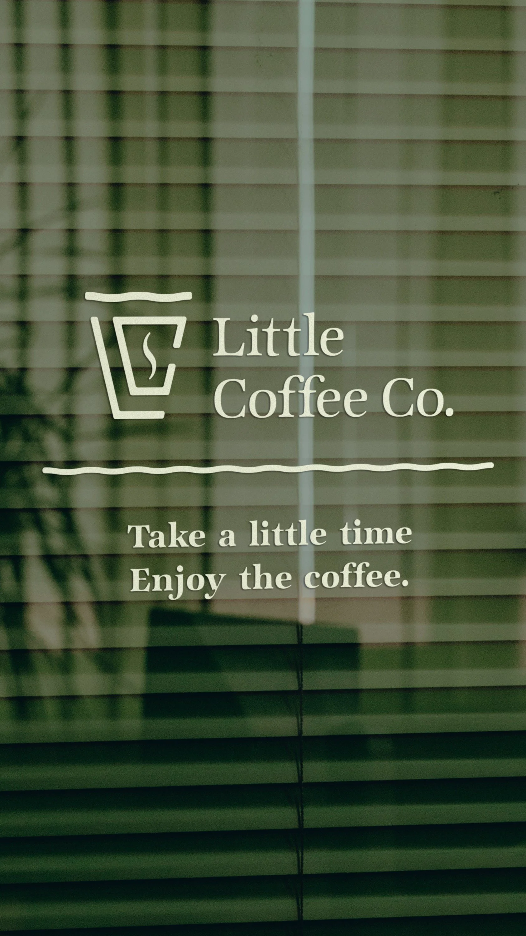 Sign for Little Coffee Co. with a coffee cup icon, suggesting taking time to enjoy coffee, placed on a window with horizontal blinds.