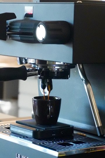 A close-up of an espresso machine pouring coffee into a black mug.