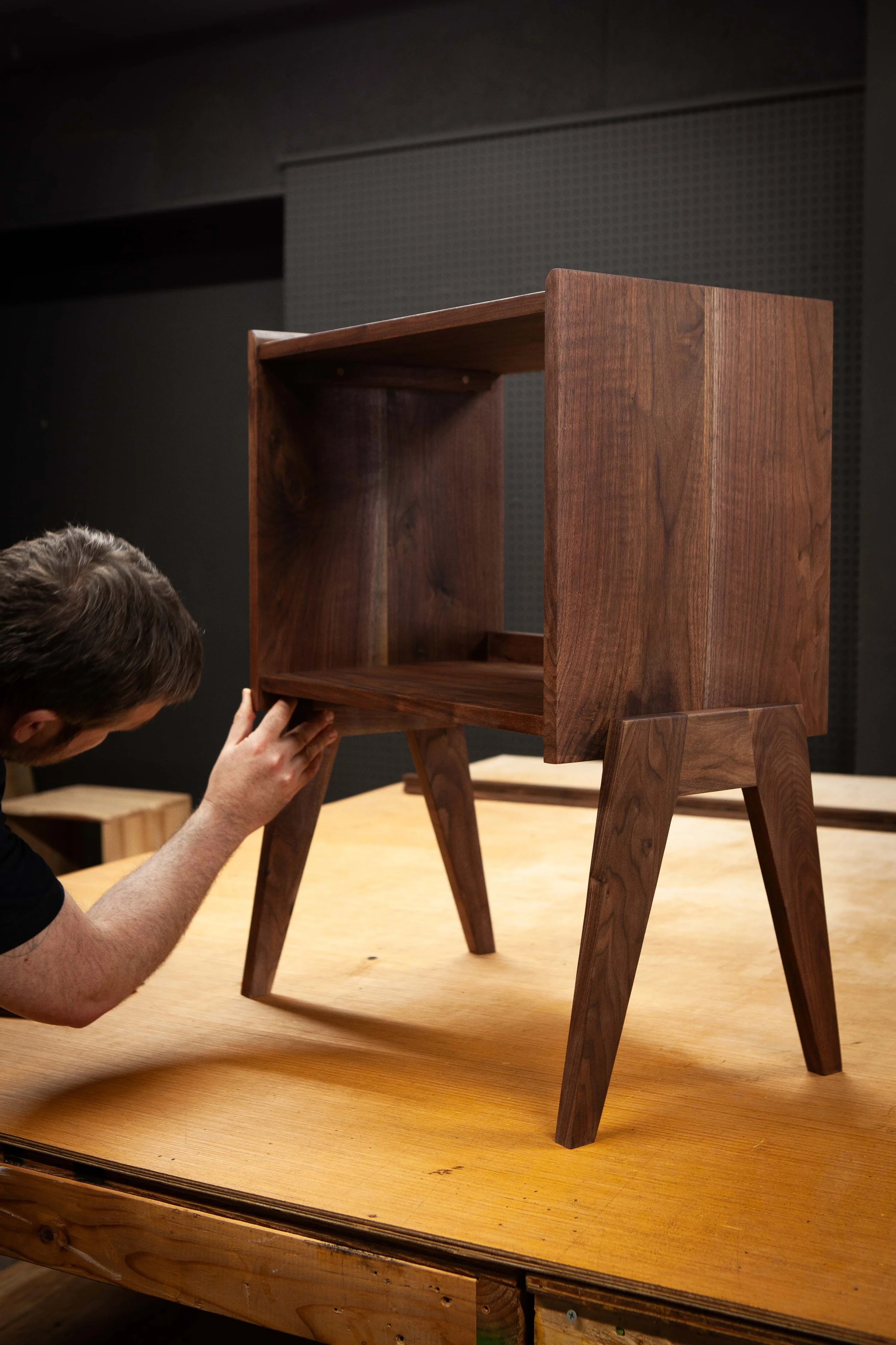 A man adjusting a wooden chair held upside down on a table in a workshop or showroom.
