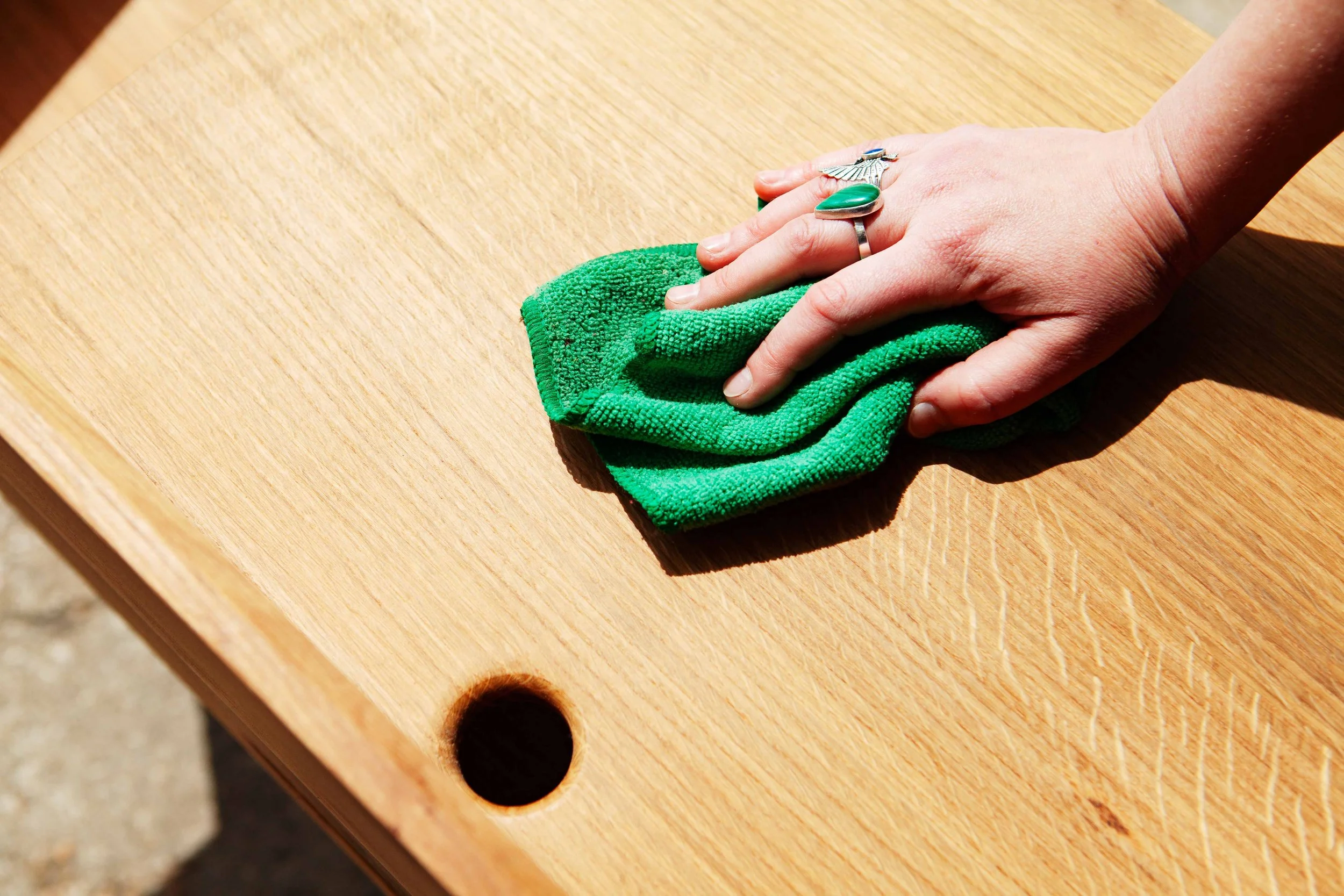 Close-up of a hand cleaning a wooden table with a green cloth.