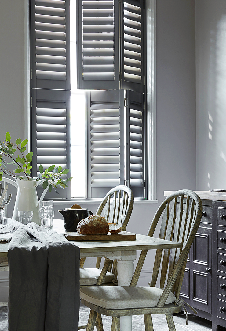 Patoma grey Faux Wood Composite tier-on-tier window shutters in a traditional dining room, featuring independently opening upper and lower panels with adjustable louvres for flexible privacy and natural light control.