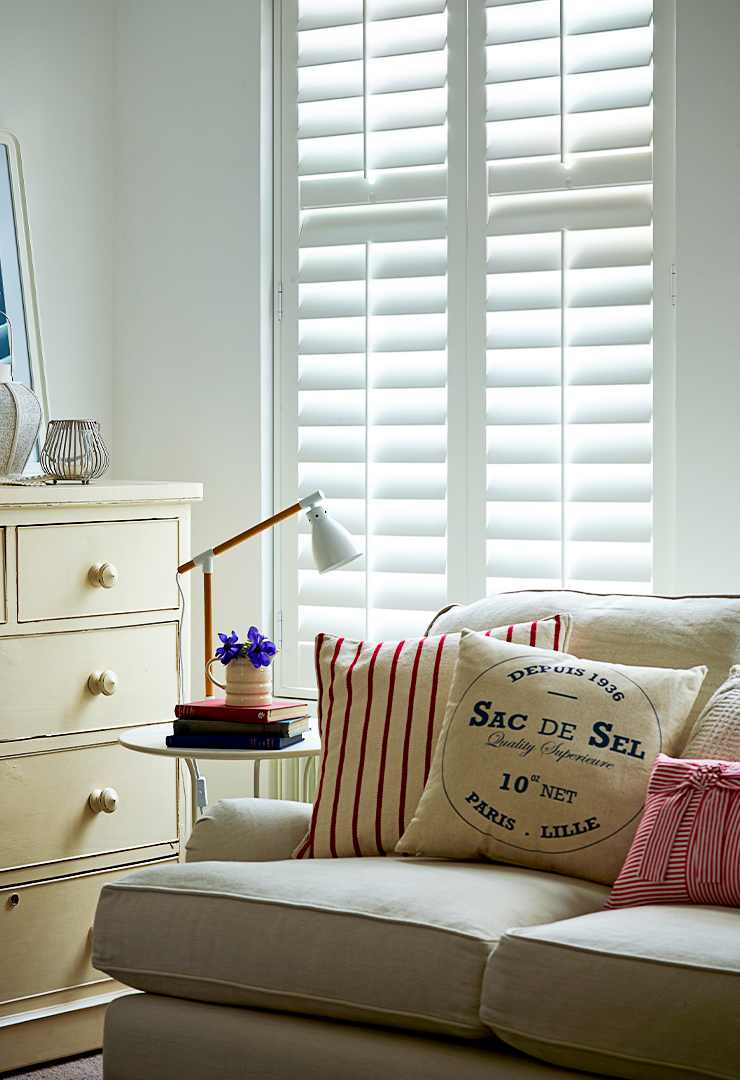 Patoma Basswood hardwood full height window shutters in a bright contemporary living room, featuring a smooth painted white finish and adjustable louvres for privacy and natural light control.