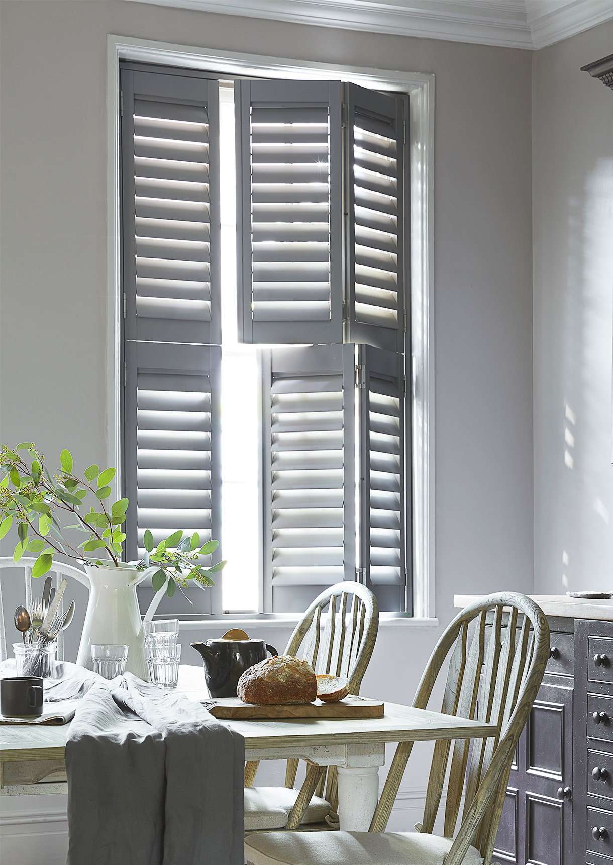 Grey tier-on-tier window shutters with independently opening upper and lower panels in a dining room.