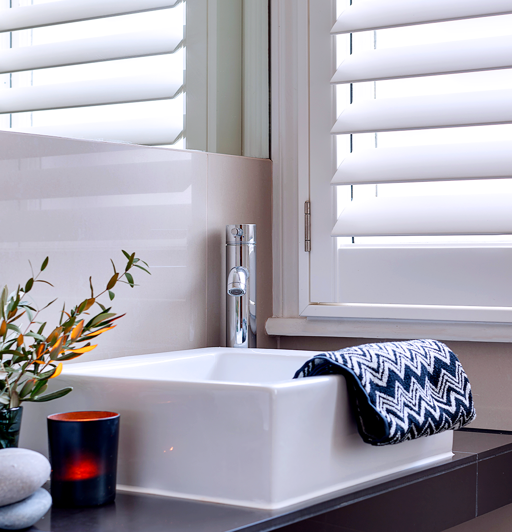 Patoma white Polyvinyl composite café style window shutters above a contemporary bathroom sink, featuring waterproof construction and adjustable louvres for privacy, natural light control and moisture-resistant performance.