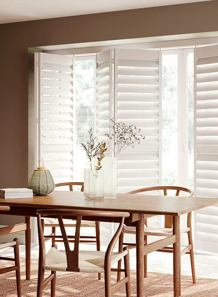 White tracked window shutters with wide louvres fitted across large dining room windows.