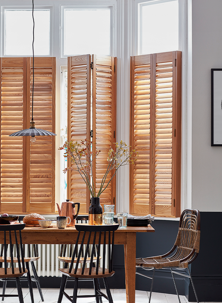 Natural wood café style window shutters with open louvres fitted to tall dining room windows.