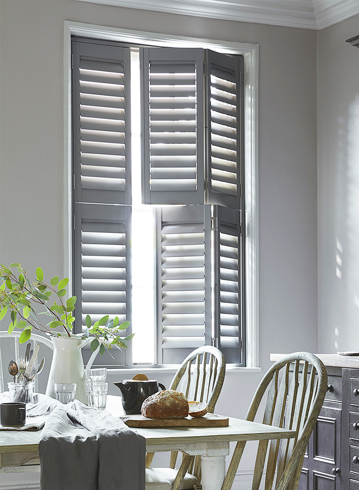 Grey tier-on-tier window shutters with independently opening upper and lower panels in a dining room.