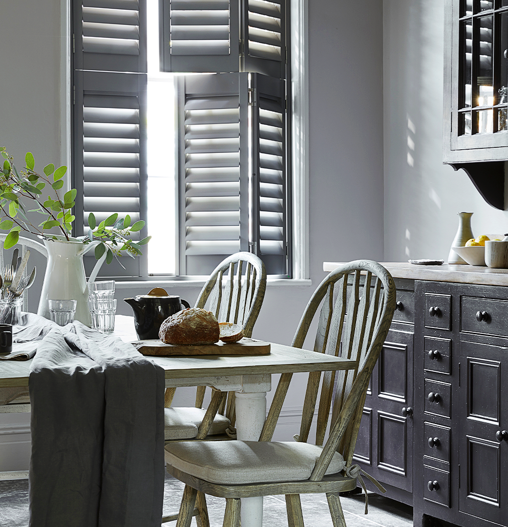 Patoma grey Faux Wood Composite tier-on-tier window shutters in a traditional dining room, featuring independently opening upper and lower panels with adjustable louvres for flexible privacy and natural light control.
