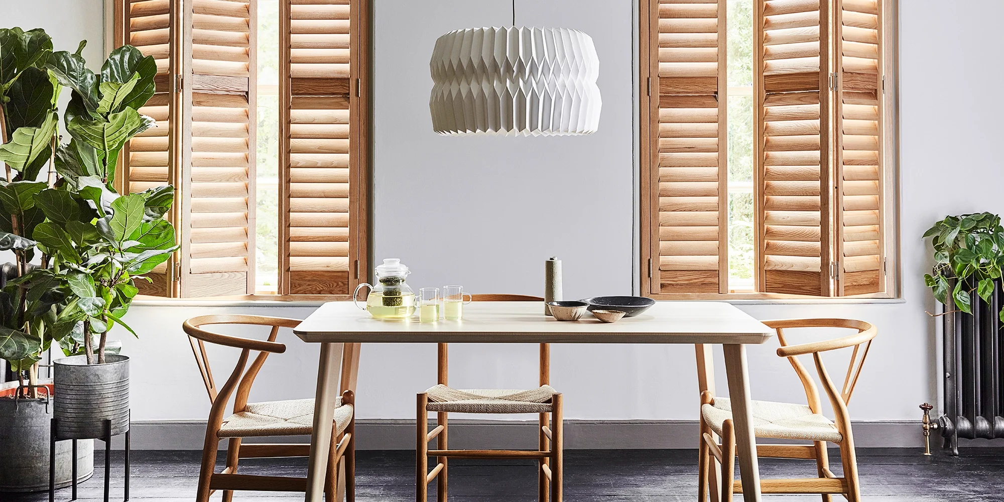 Natural hardwood plantation shutters fitted to tall dining room windows, showing the distinctive wood grain and warm natural finish.
