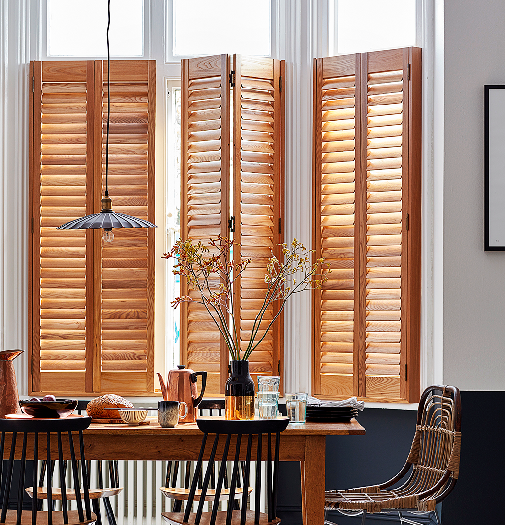 Patoma Paulownia hardwood café style window shutters in a contemporary dining room, featuring a warm natural wood finish, visible timber grain and adjustable louvres for privacy and natural light control.
