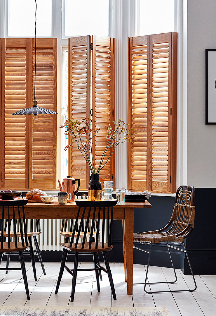 Patoma Paulownia hardwood café style window shutters in a contemporary dining room, featuring a warm natural wood finish, visible timber grain and adjustable louvres for privacy and natural light control.