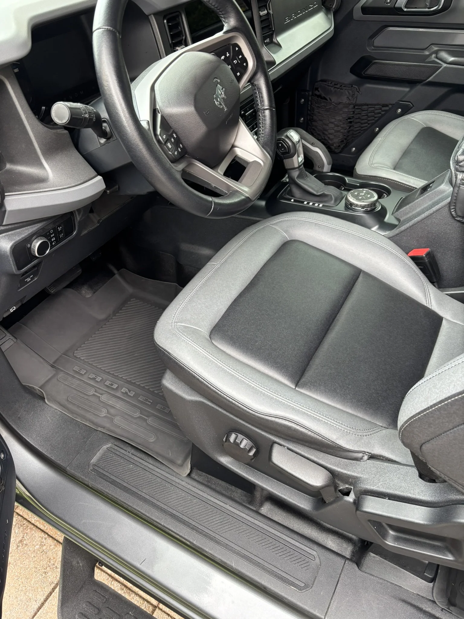 Interior of a vehicle, showing a black steering wheel with the vehicle emblem, gear shift, control knob, and part of the driver and passenger seats.