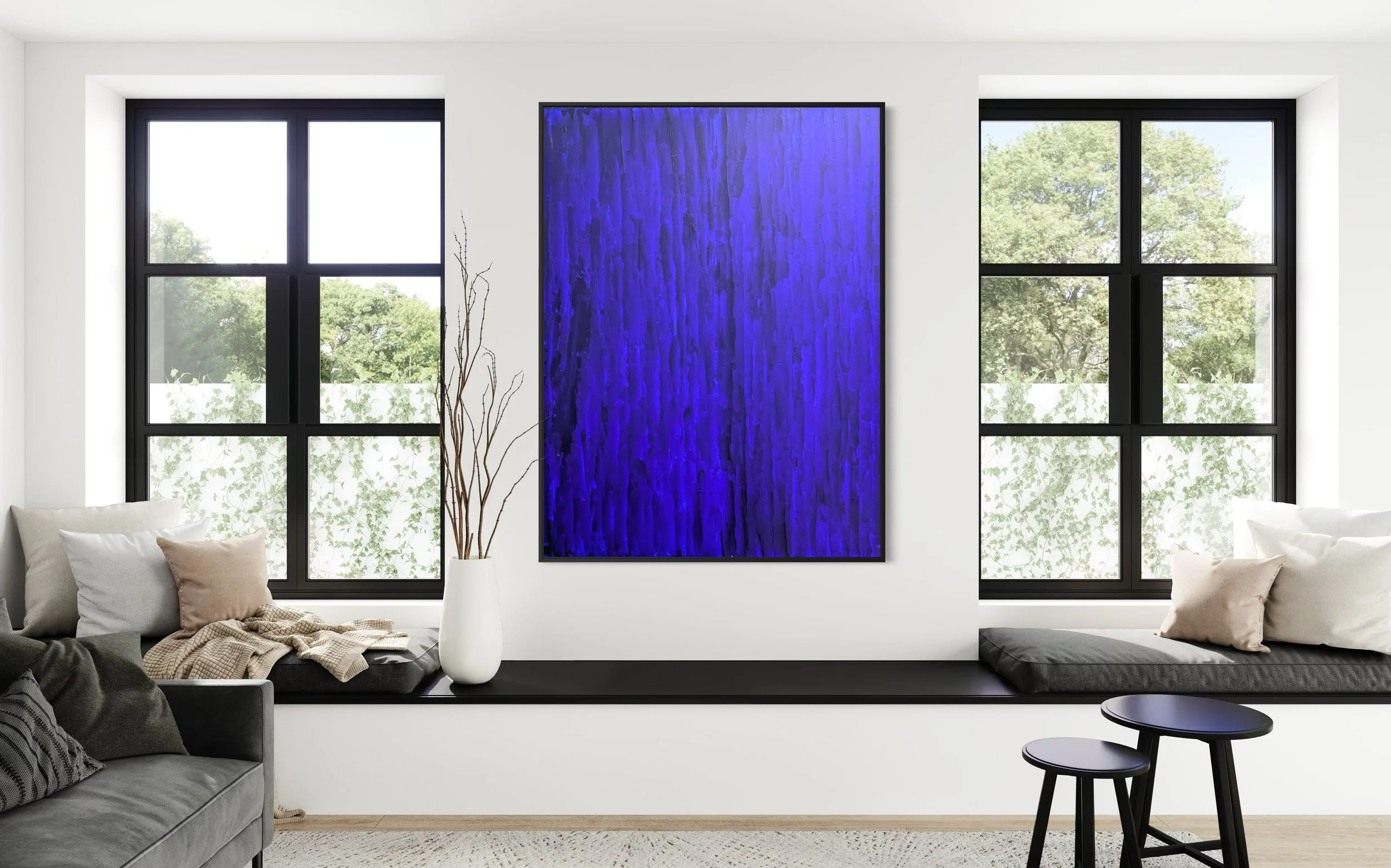 Modern living room with large black-framed windows, white walls, blue textured wall artwork THE BLUE by Paul Bell, beige and grey cushions, a tall white vase with branches, a grey sofa, and black side tables.