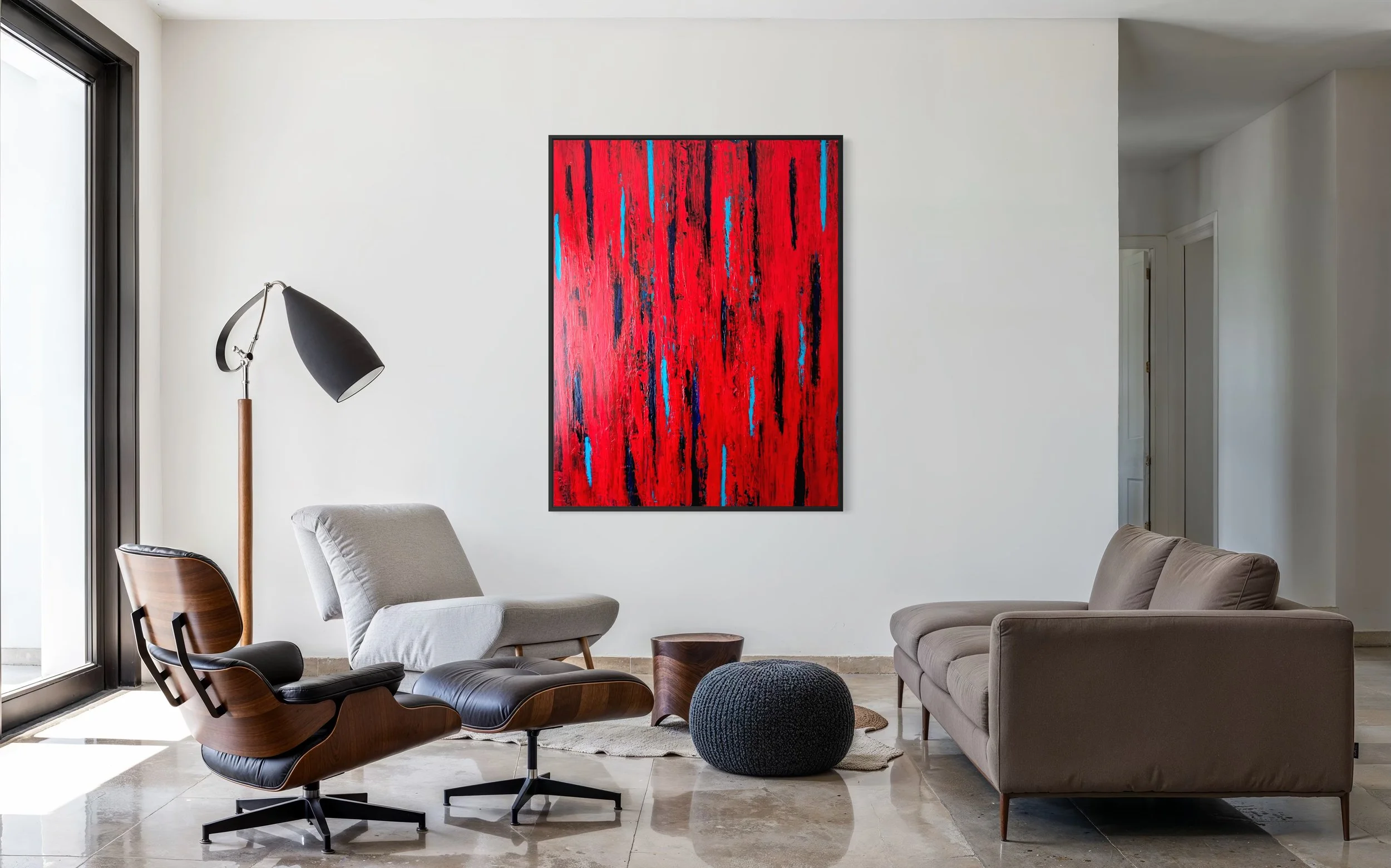 Modern living room with white walls, a colourful red and blue abstract painting, AWAKENING by Paul Bell, a black floor lamp with a wood stand, a grey armchair, a beige sofa, and a round woven ottoman near a sliding glass door.