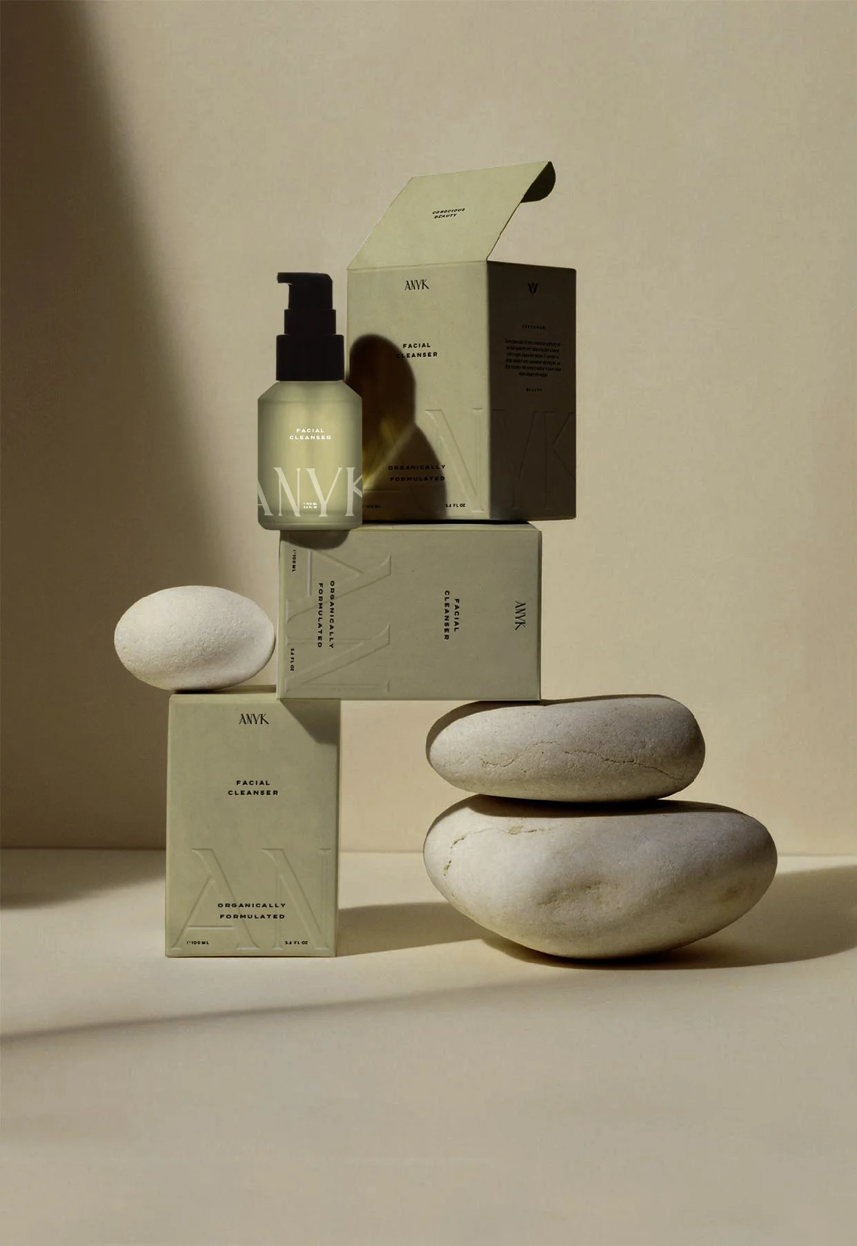 Arrangement of skincare products, including face cleanser bottles and boxes, stacked on white stones against a beige background.