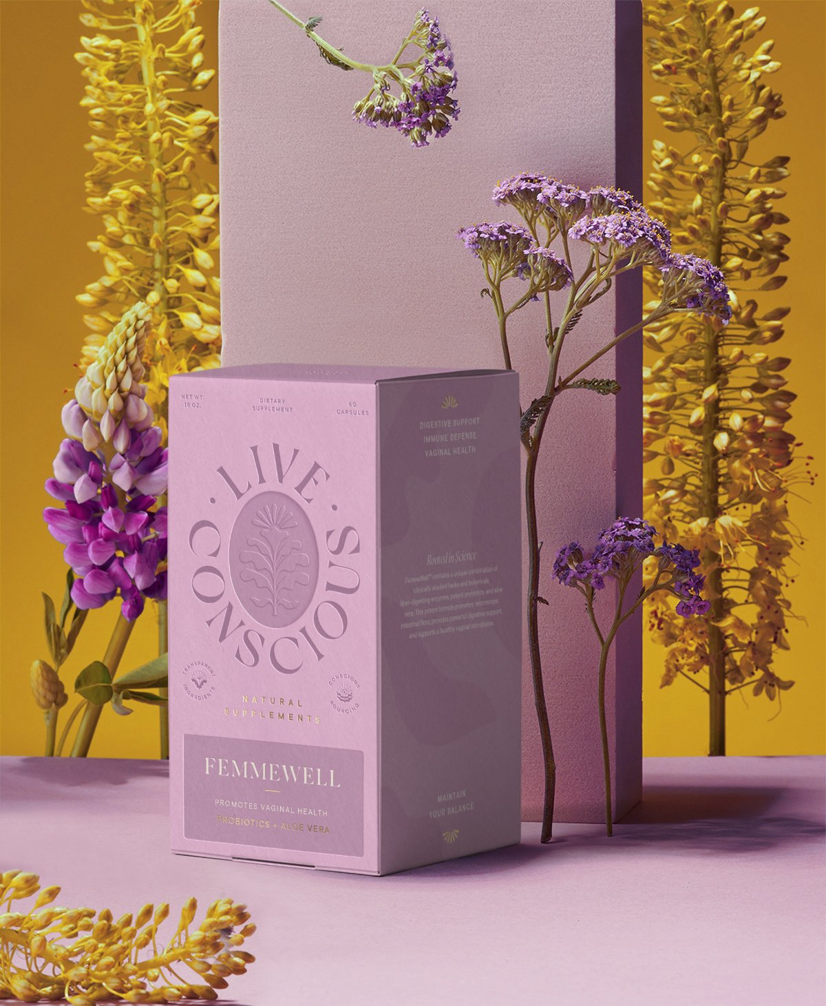 A pink box labeled 'Live C!ndusco' stands on a pink surface, surrounded by purple and yellow flowers against a colorful background. The box contains dietary supplements promoting vaginal health, probiotics, and aloe vera.