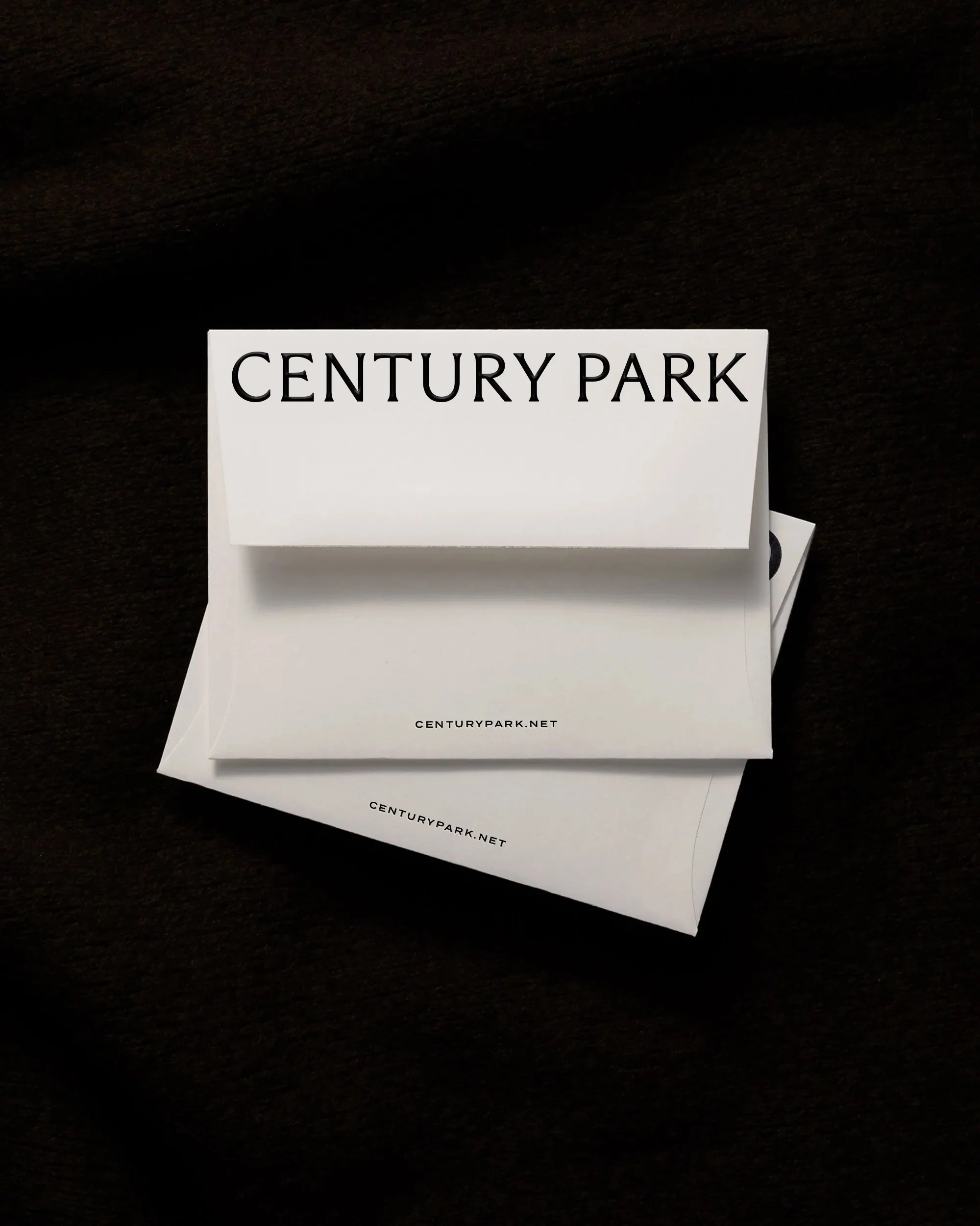 Close-up of a white paper or card with the text 'CENTURY PARK' printed in black, placed on a dark surface with additional similar paper beneath it.