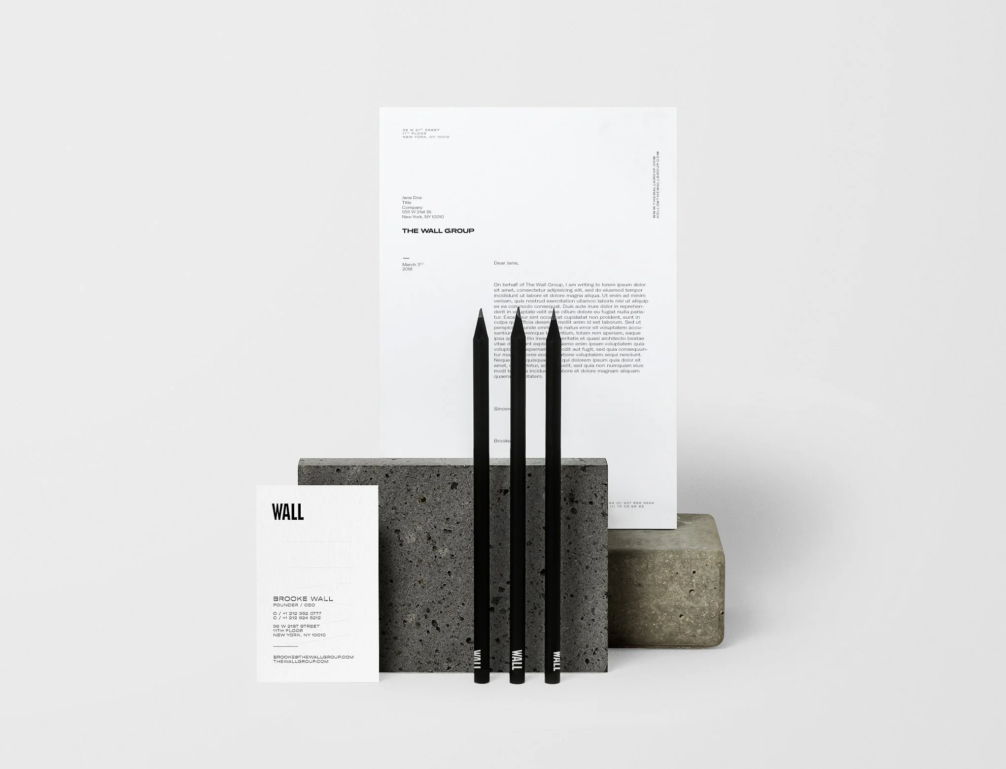 White business stationery with black text, three black pens, and three concrete blocks on a white surface.