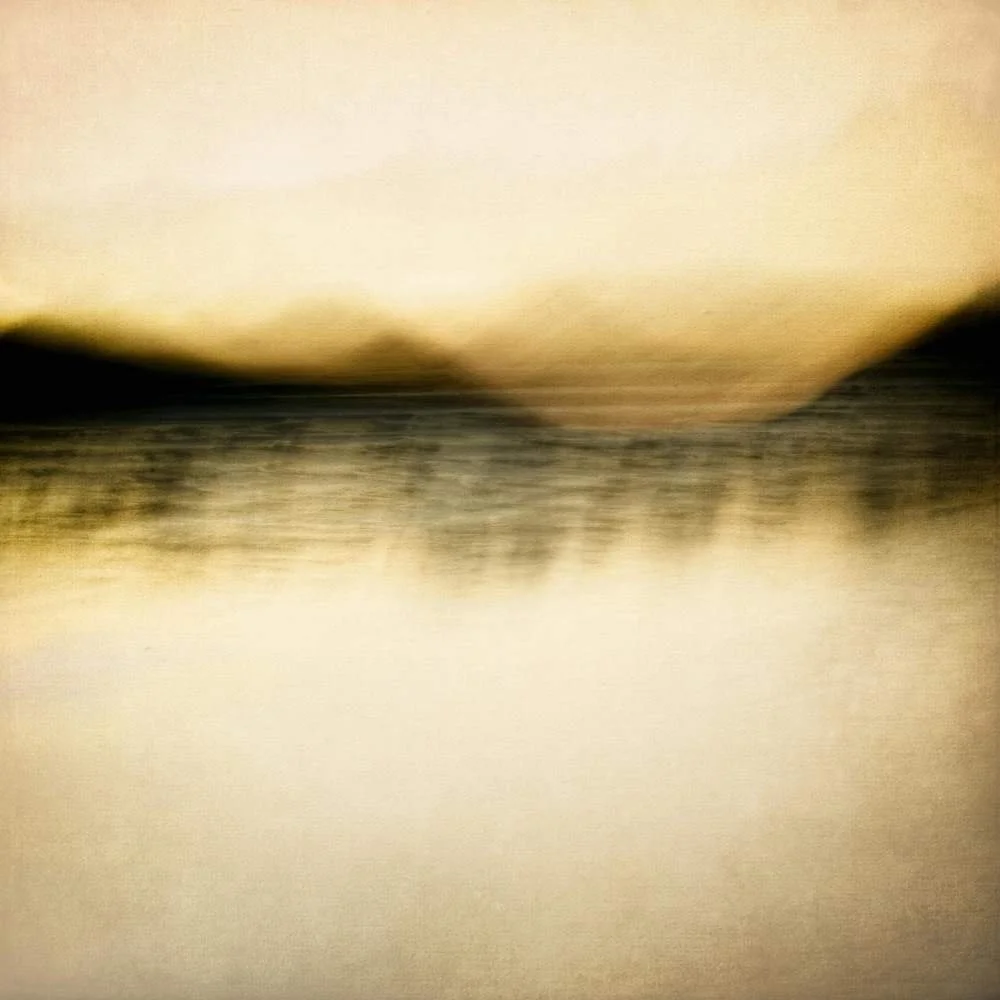 Abstract, blurry image of water with a horizon and mountains in the background, sunset or sunrise lighting.