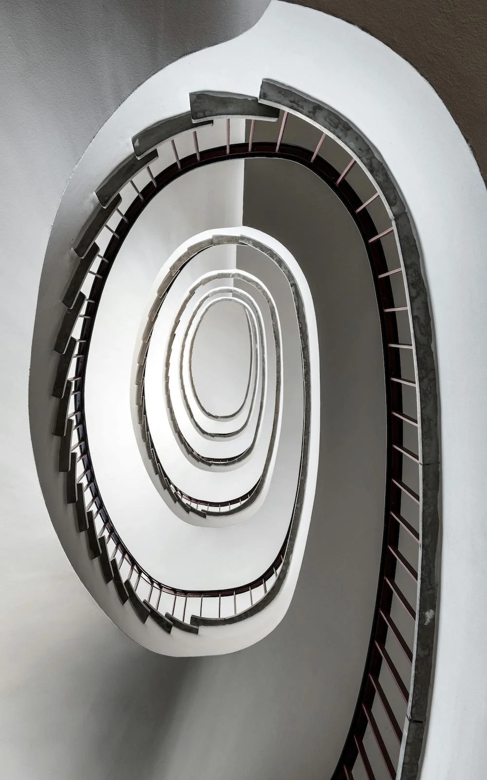 View of a spiral staircase from above, featuring metal handrails and white walls, creating a concentric pattern.