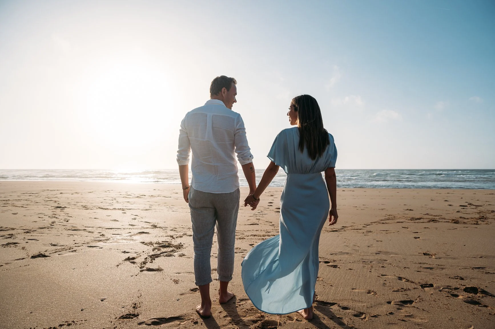 A couple walking hand in hand on a sandy beach during sunset.