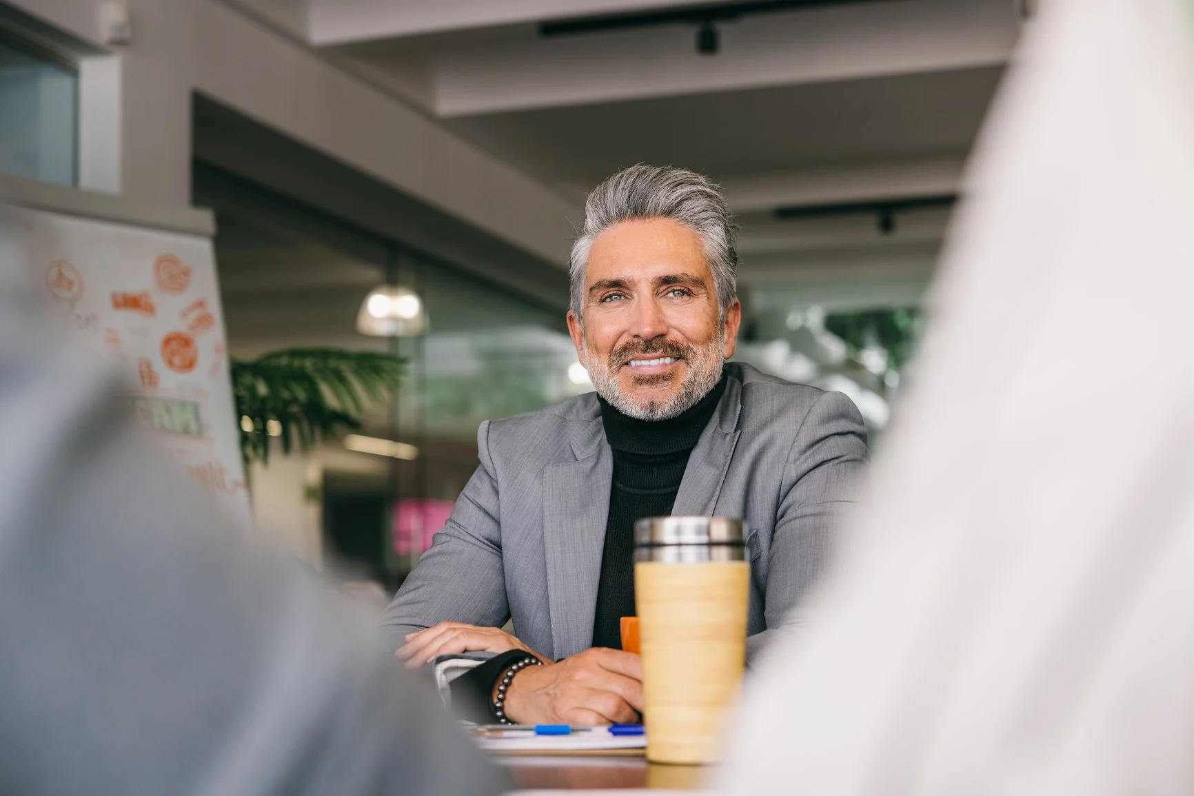 A smiling middle-aged man sitting at a table in a modern cafe.