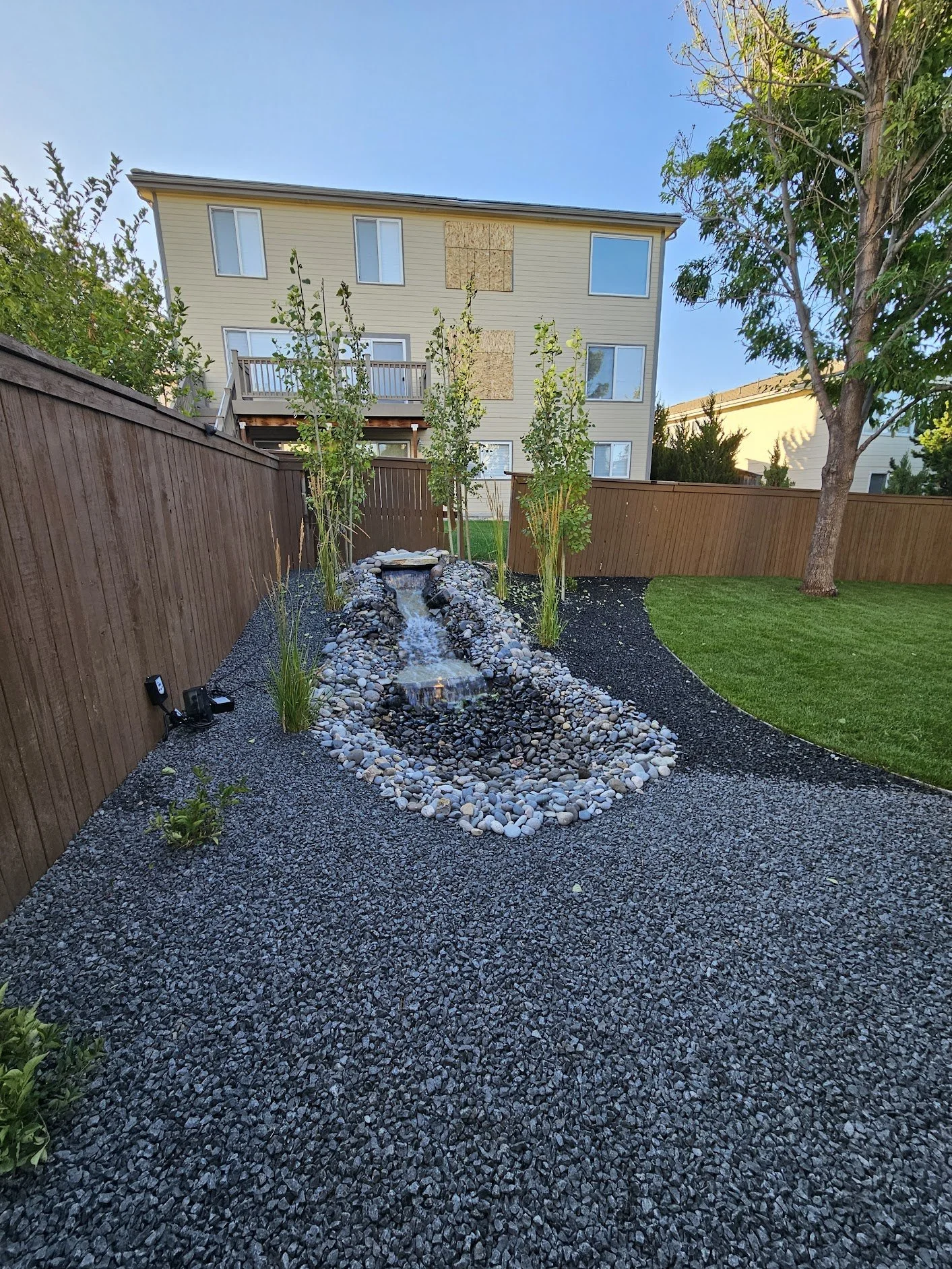 Pondless water feature with black granite and river rock cobble surrounded by Aspen trees and fountain grasses