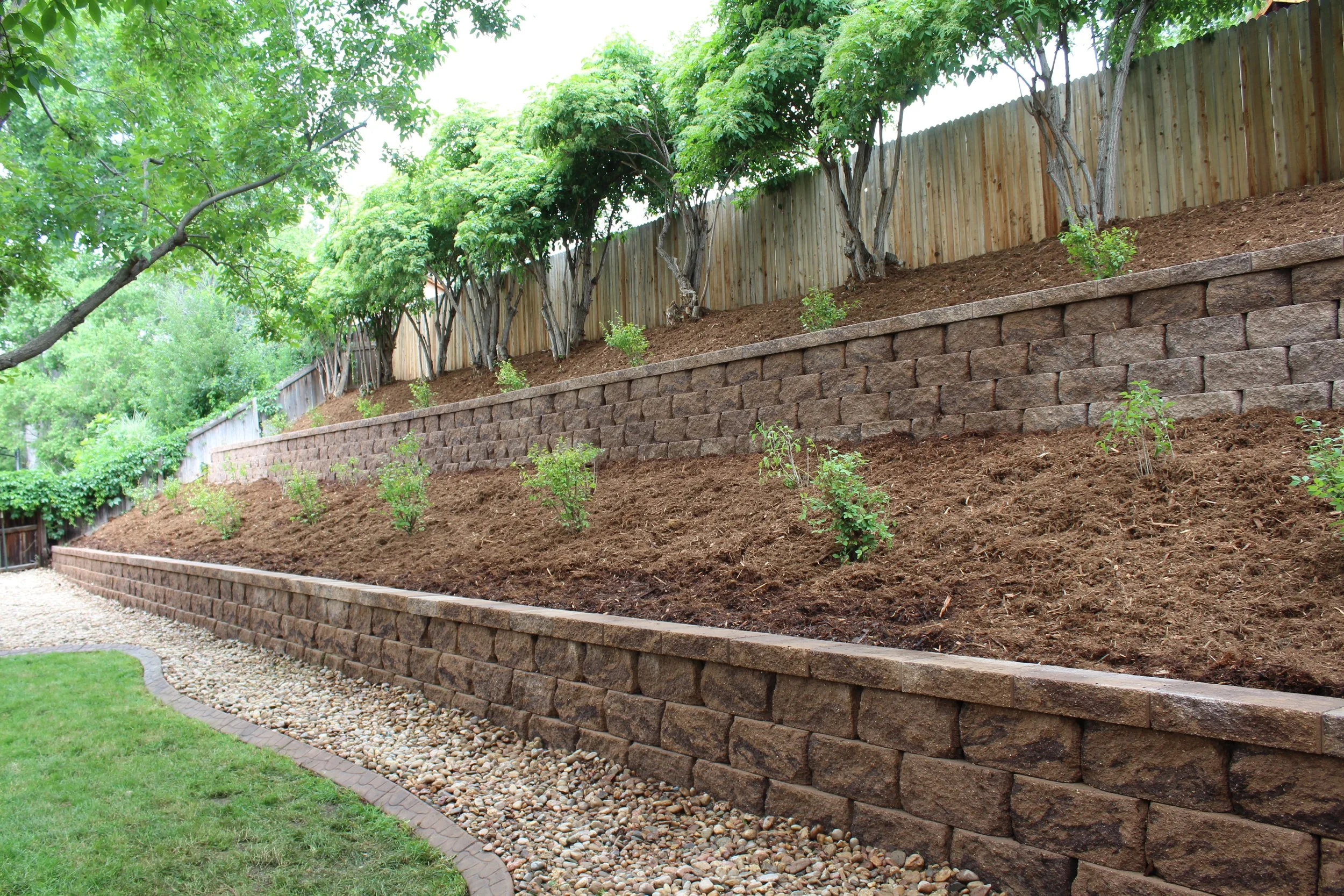 Morrison back yard double tiered retaining wall with cap and planted with lilacs and mulch