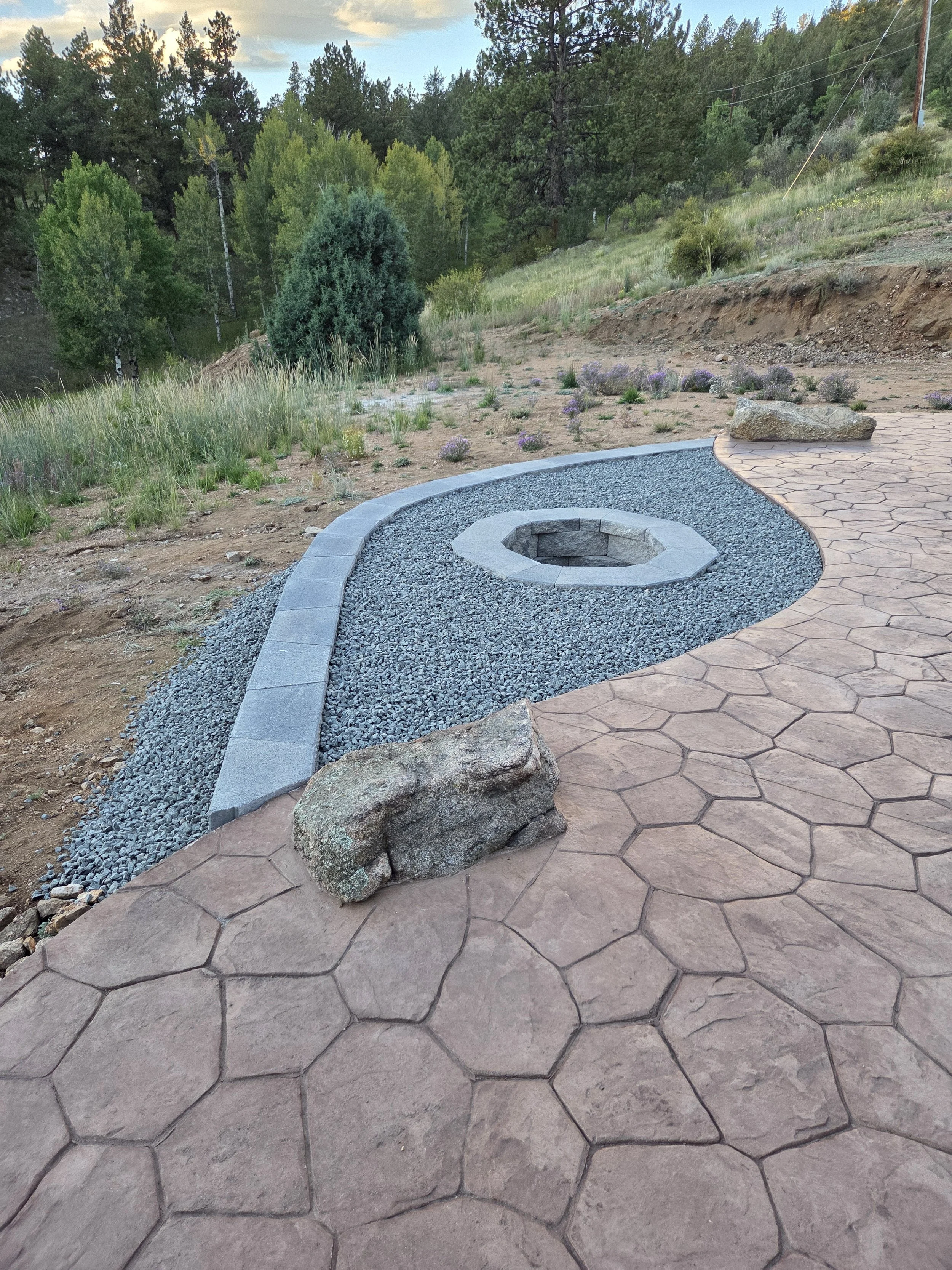 Recessed wood burning fire pit with concrete patio and moss rock boulders