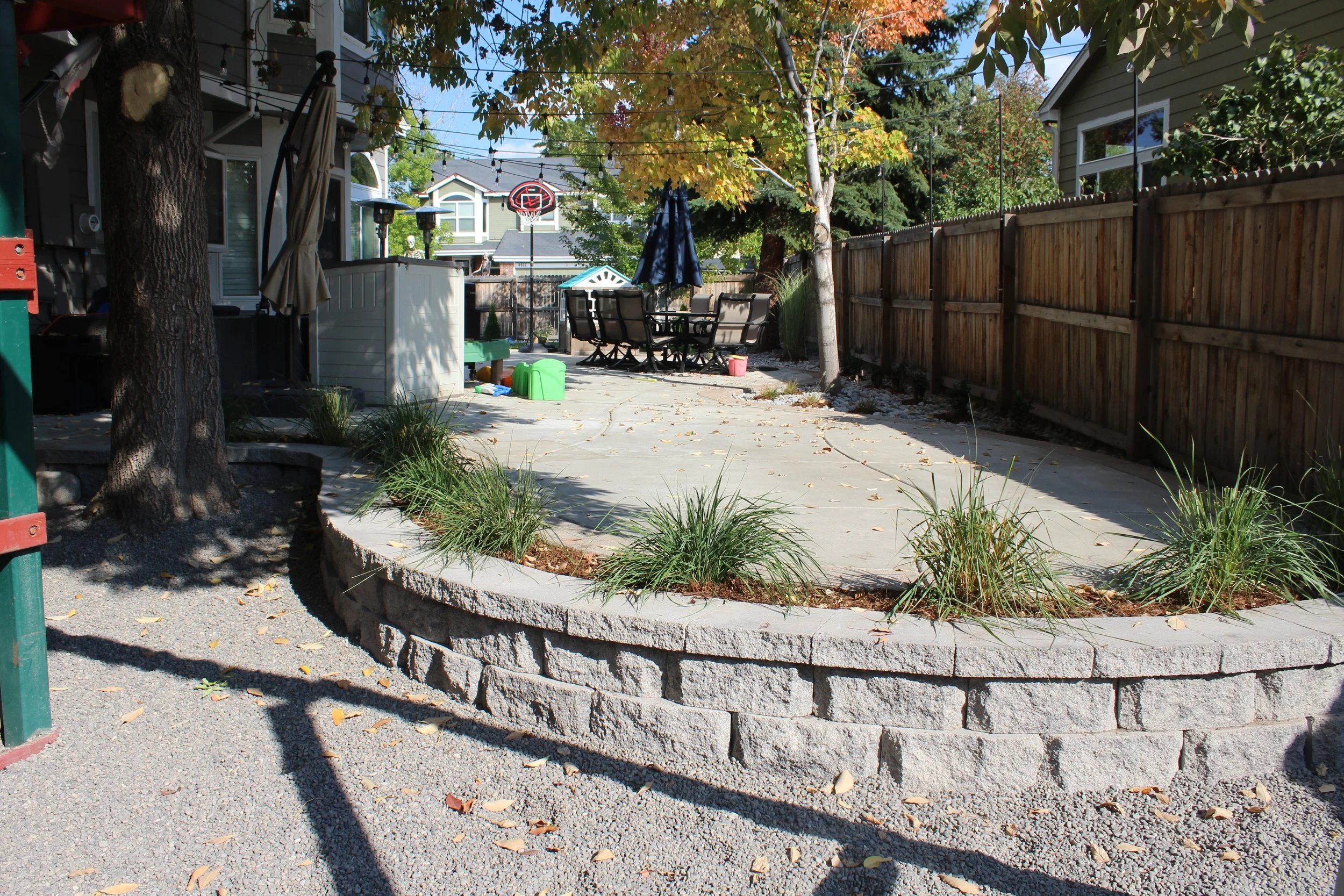 Retaining wall block and cap planter on side of concrete patio with small grasses and mulch