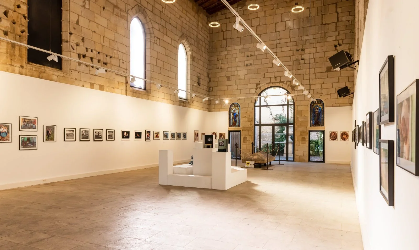 Une galerie d'art avec des œuvres accrochées sur les murs, des vitraux colorés, et des sculptures exposées au centre.