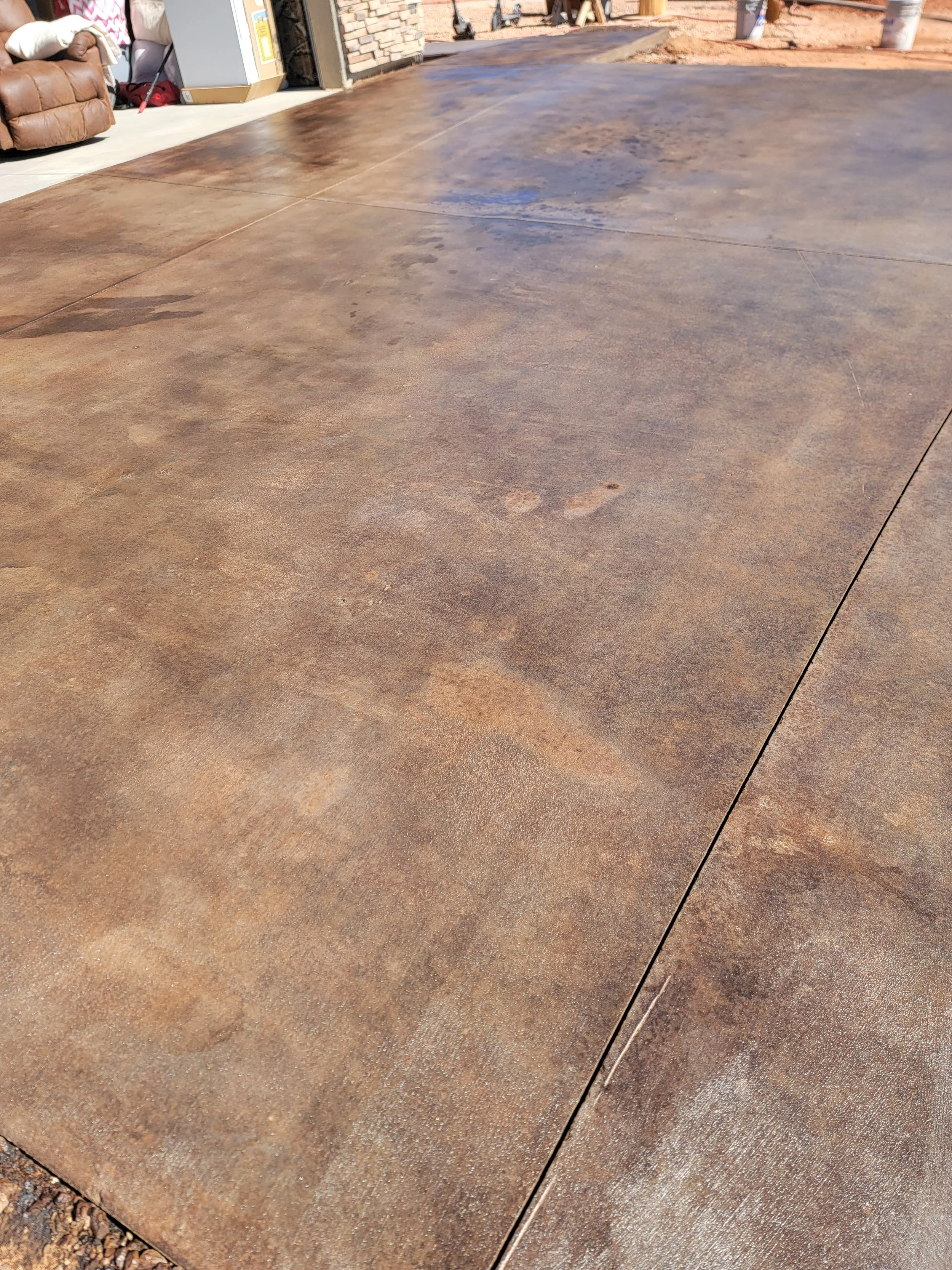 Close-up of a freshly poured concrete floor in front of a garage, with visible lines between sections and some water or stain marks on the surface.