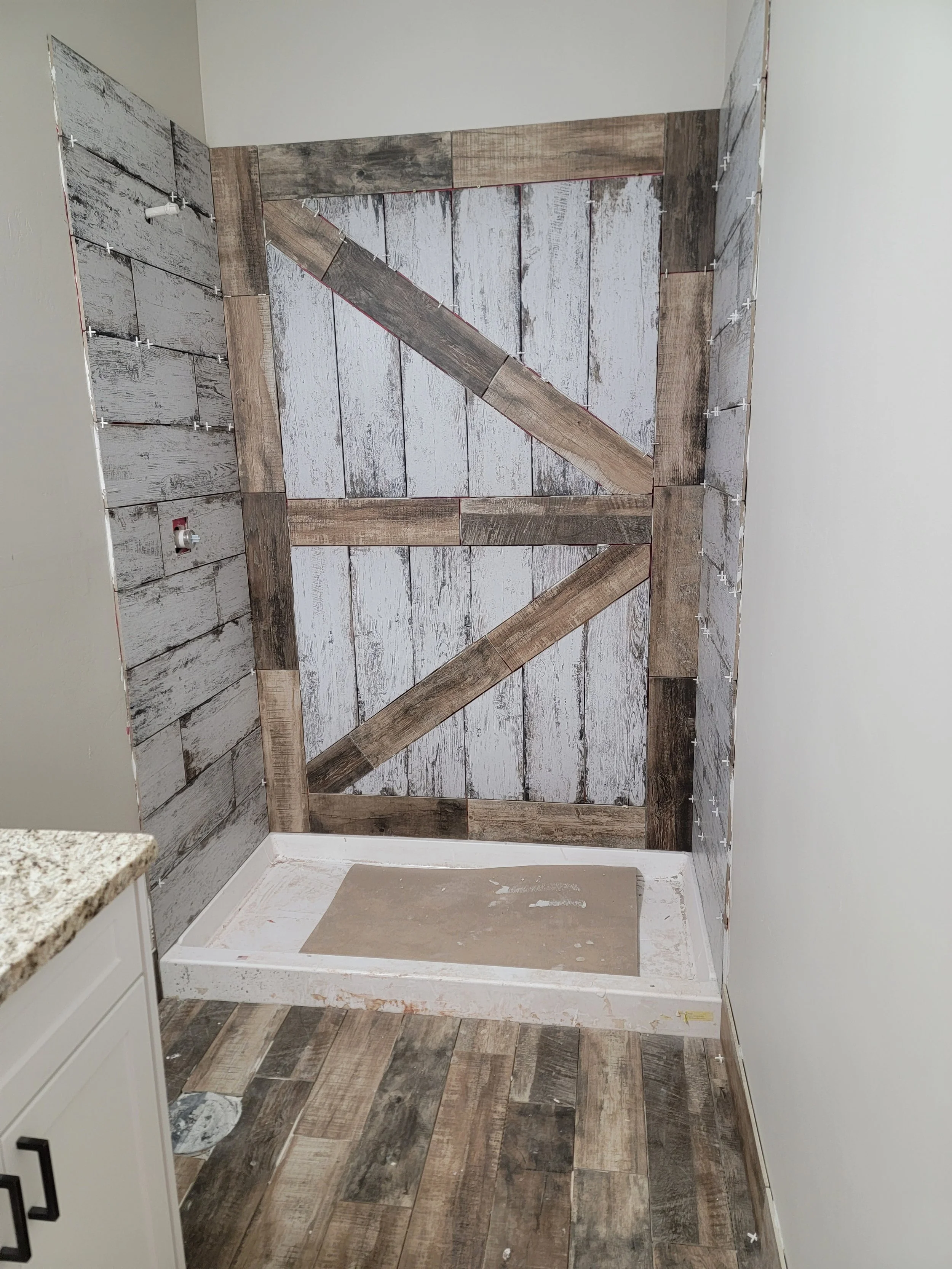 Bathroom with partially tiled wall, incomplete shower base, and tile spacers on the wall.