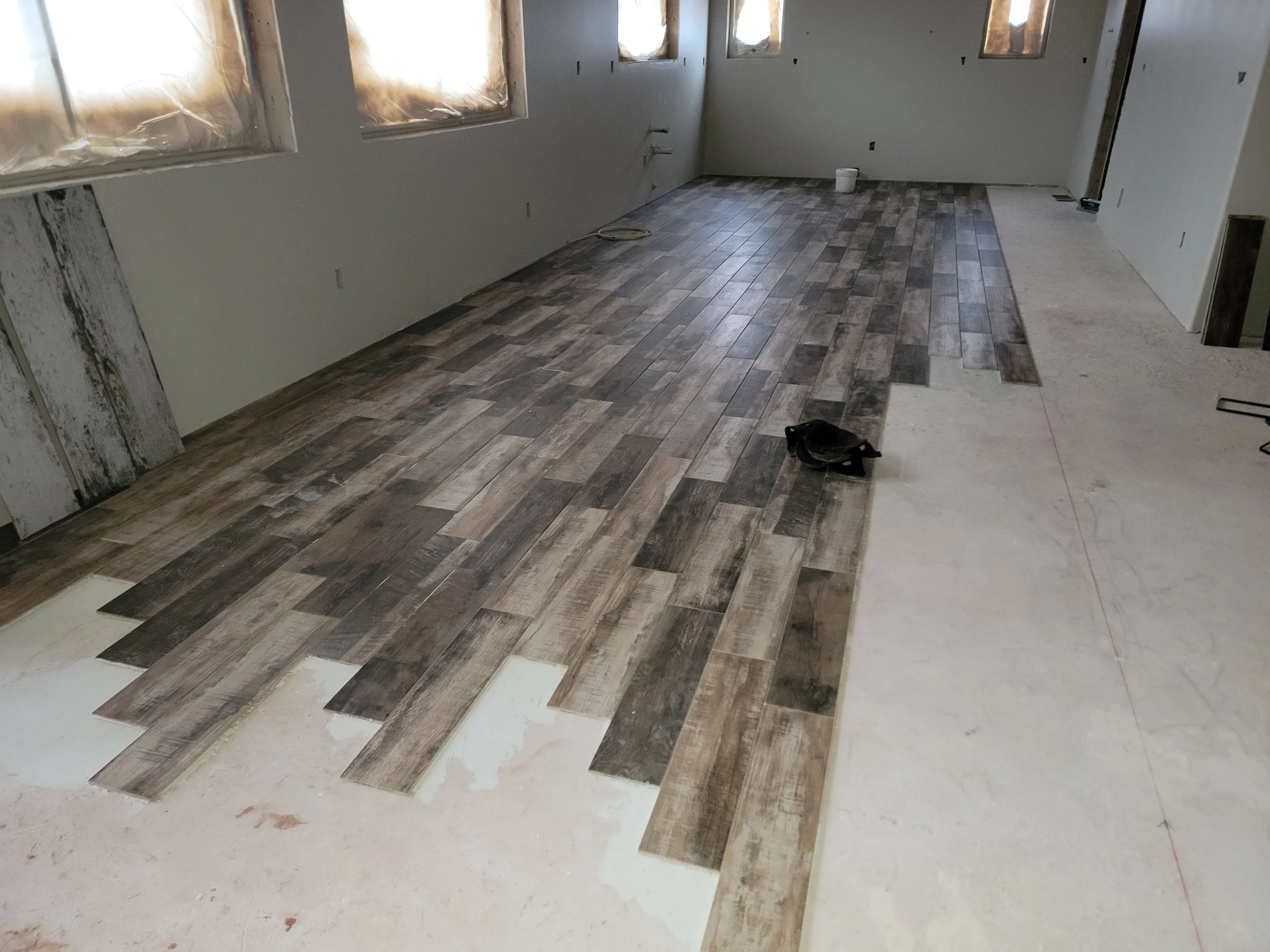 Interior of a room under construction with partially installed wood-look flooring, several windows covered with plastic, and a solitary bird on the floor.