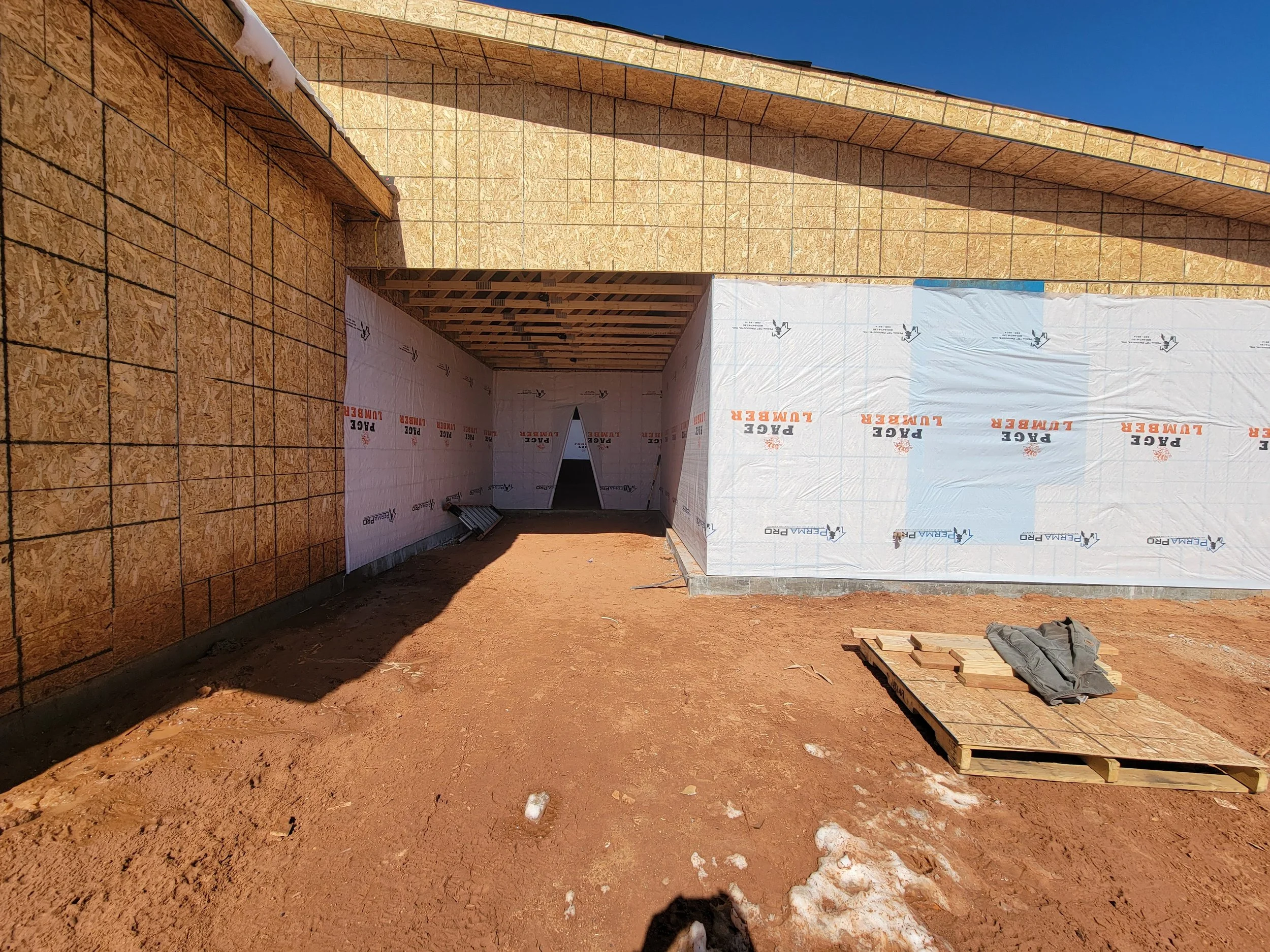 Construction site with partially built exterior walls, some covered in insulation material, and clear blue sky.