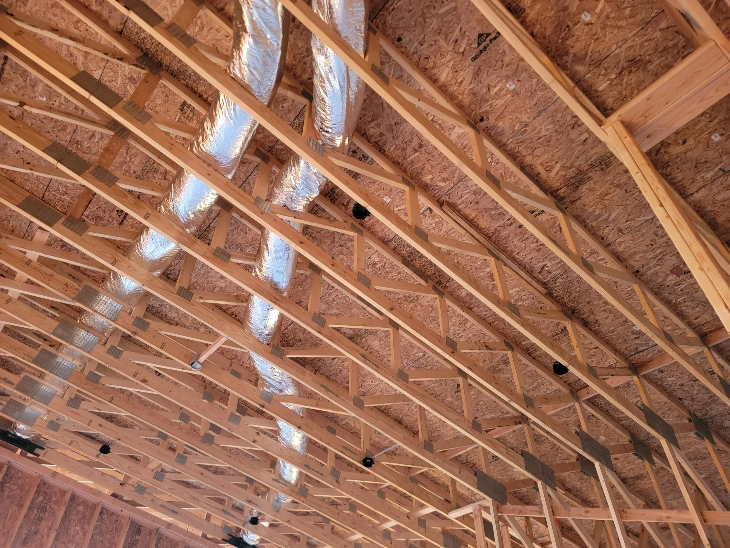 The ceiling of a building under construction showing wooden framing, silver air ducts, and insulation panels.