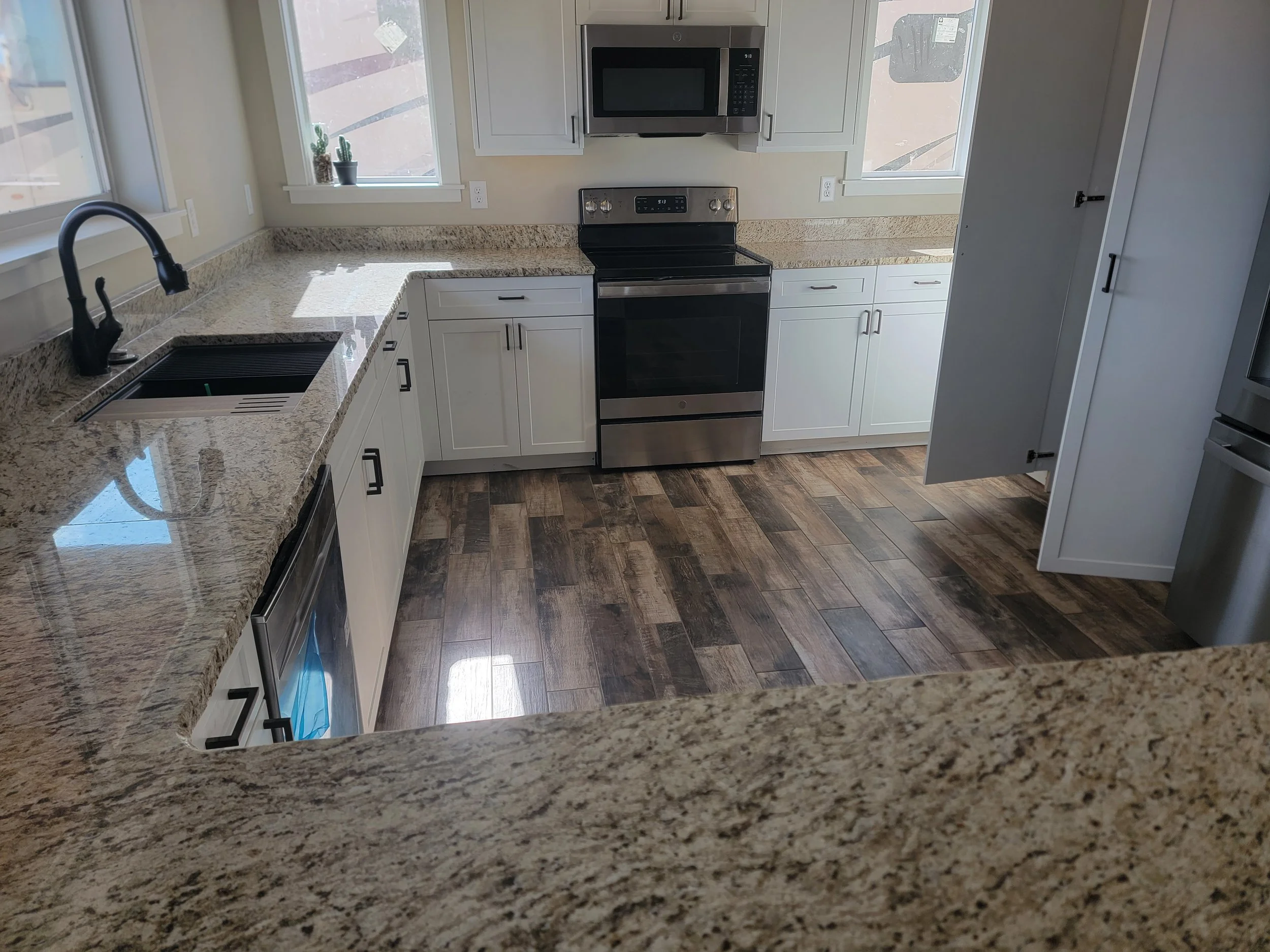 Kitchen with granite countertops, white cabinets, stainless steel appliances including microwave and oven, black faucet, and wood flooring.