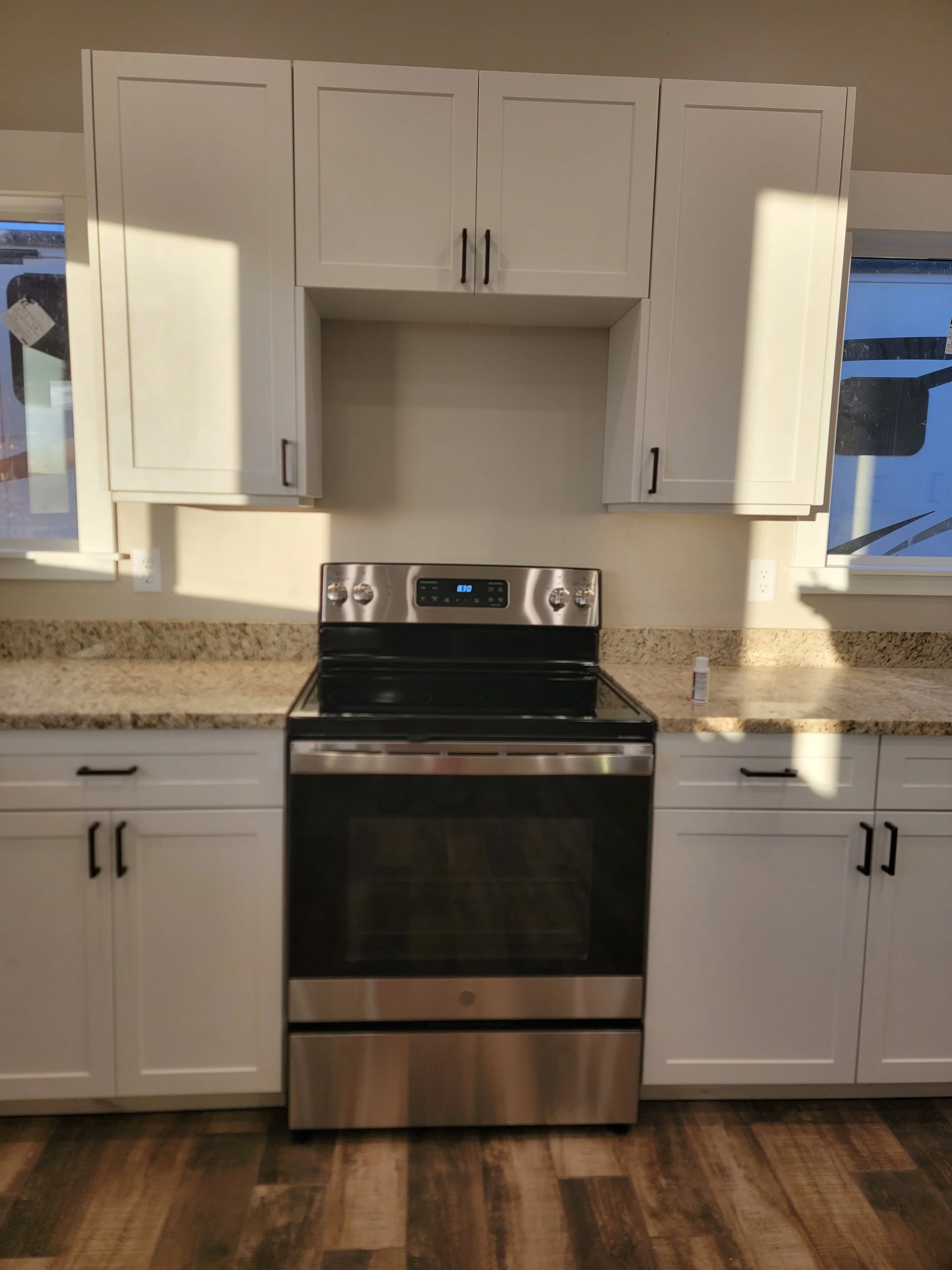 Kitchen with white cabinets, a stainless steel stove, granite countertop, and wood flooring.